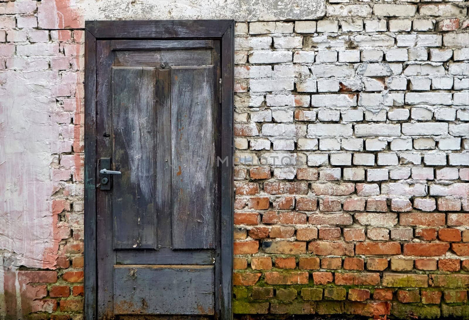 The vibrant blue wooden door, set against the weathered brick wall and adorned with remnants of whitewash, exudes a sense of history and charm, creating a timeless and welcoming atmosphere.