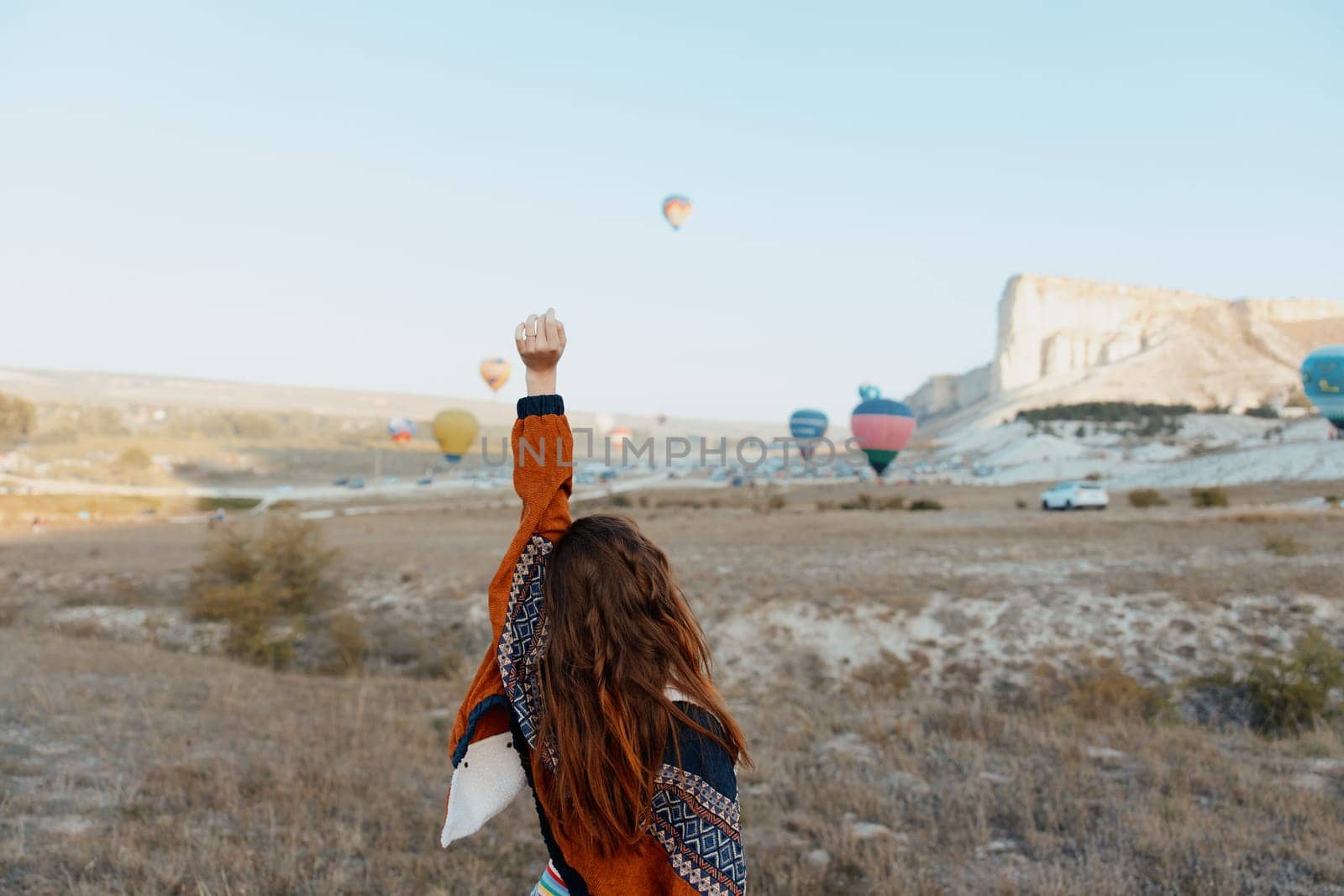 Woman in a field admiring colorful hot air balloons in the sky on a sunny day