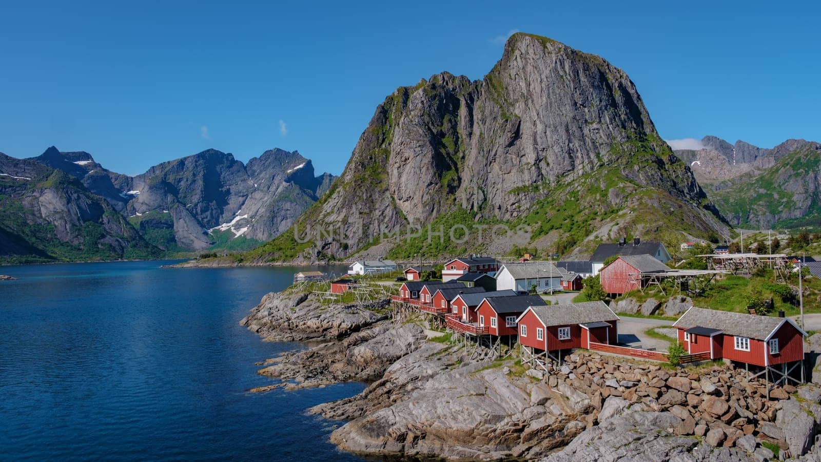 A scenic view of red cabins situated on the rocky shores of a fjord in Norway. Surrounded by towering mountains, Hamnoy fishing village on Lofoten Islands, Norway with red rorbu houses