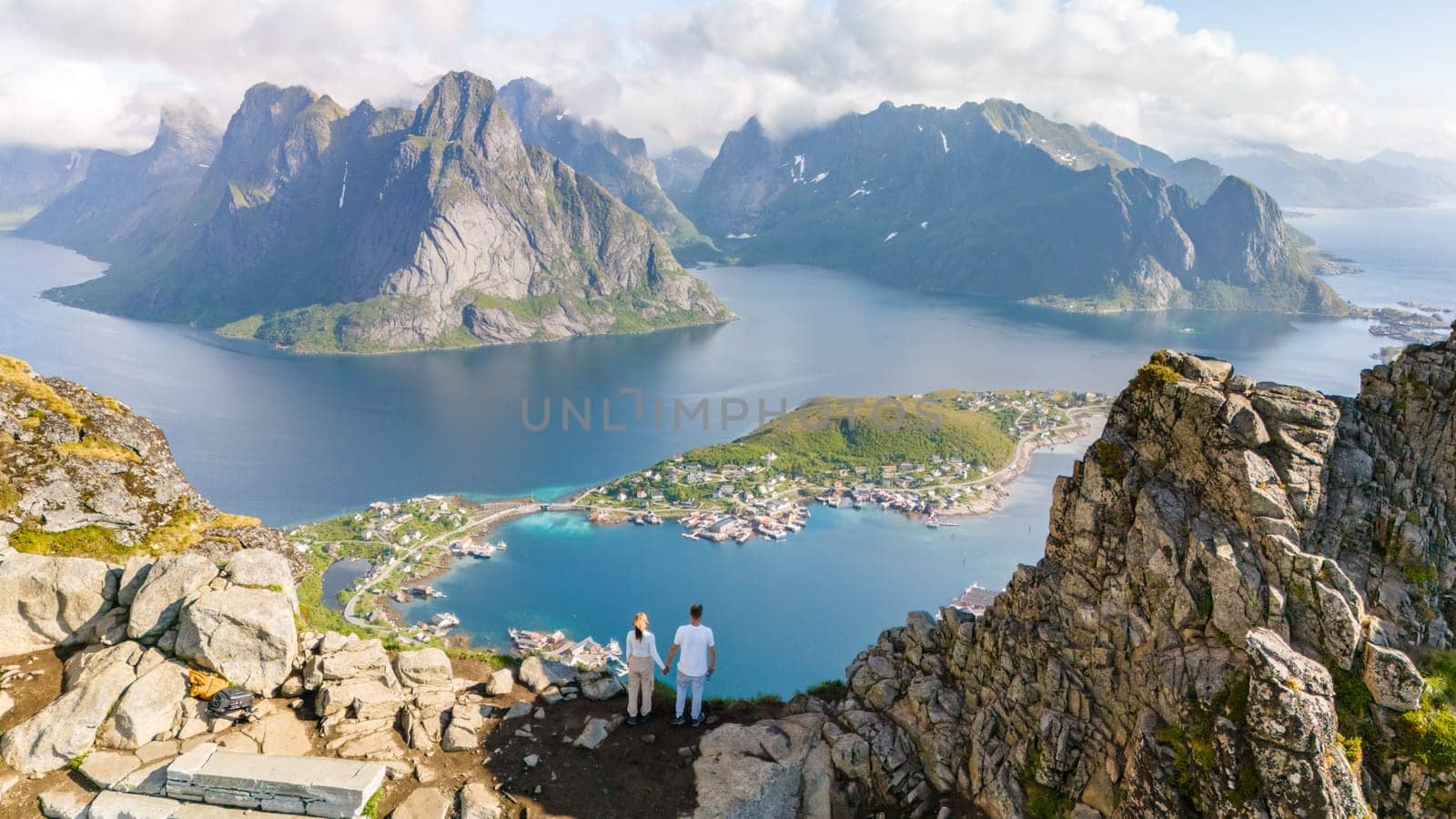 Two people stand on a rocky peak overlooking the picturesque Reinefjord in Lofoten, Norway. a diverse couple of men and women hiking the Reinebringen mountain in the Lofoten