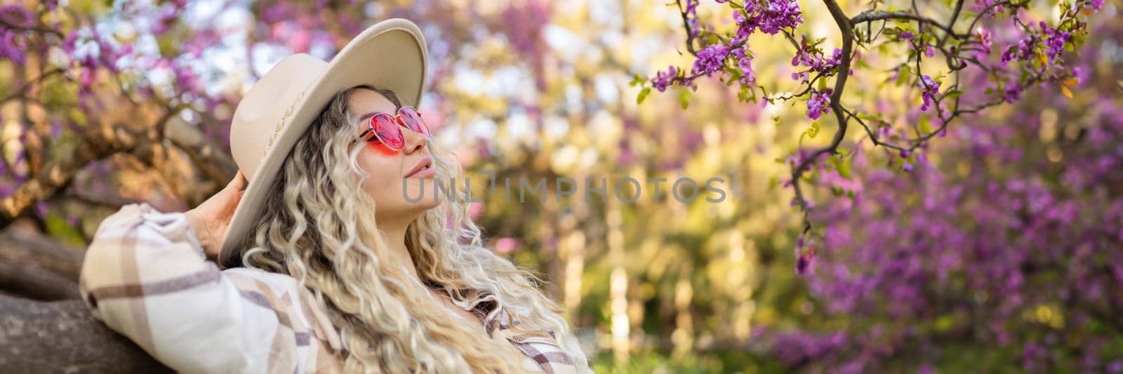 Beautiful woman in sunglasses near blossoming tree on spring day, space for text banner by malyshph