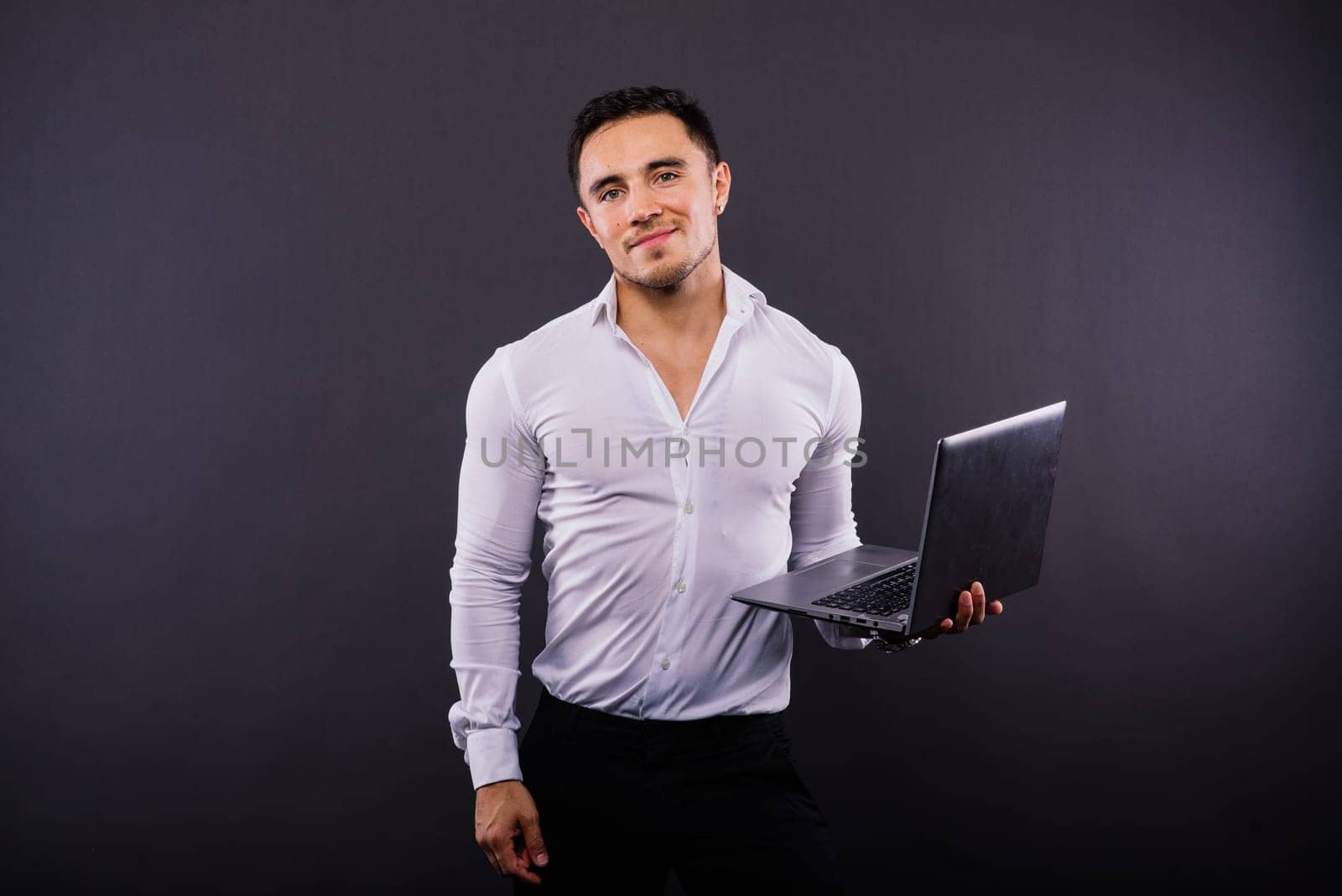 Image of young cheerful businessman holding and using laptop isolated over dark background by Zelenin