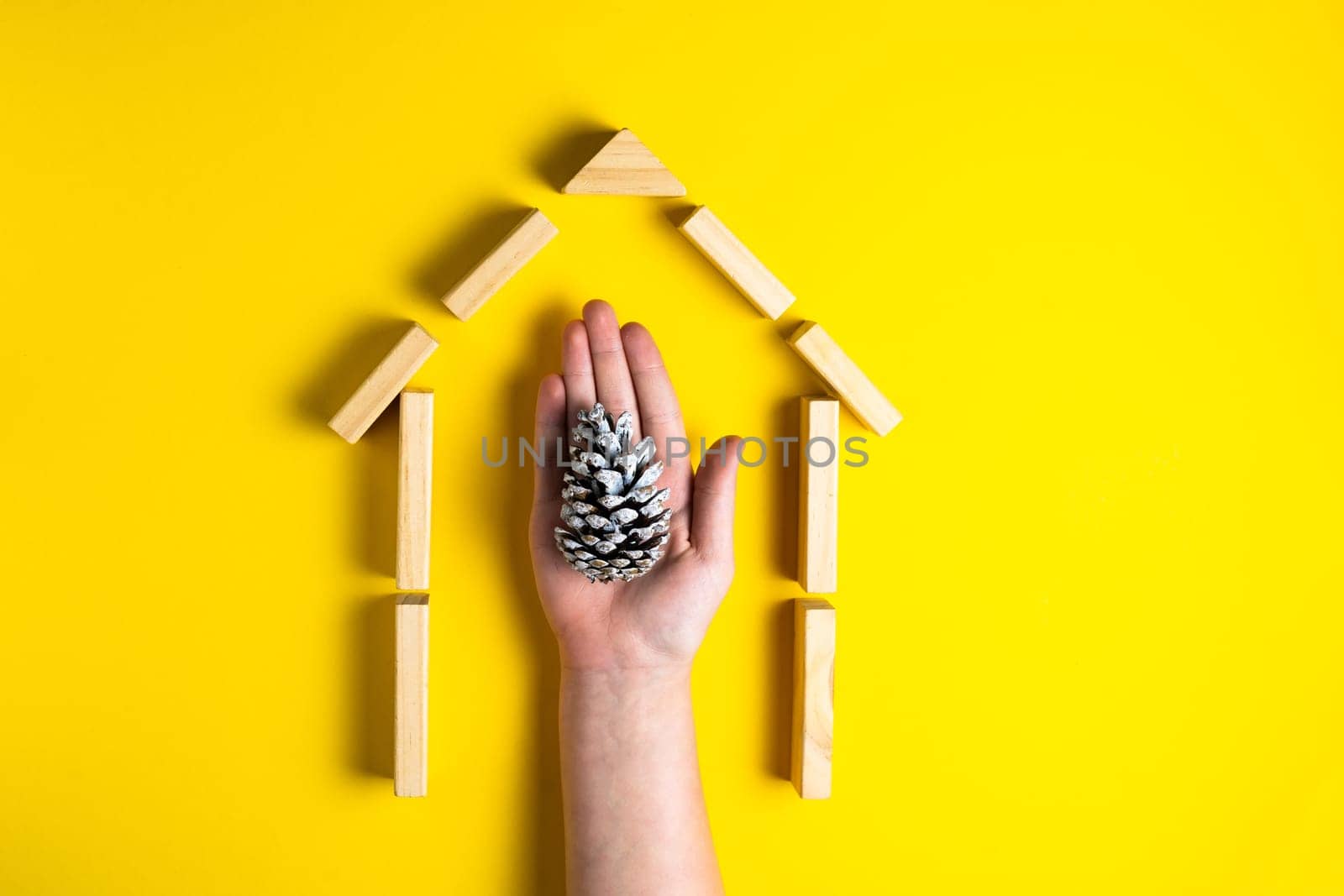 Cone with kids hand. House from wooden blocks. Close up. Top view.