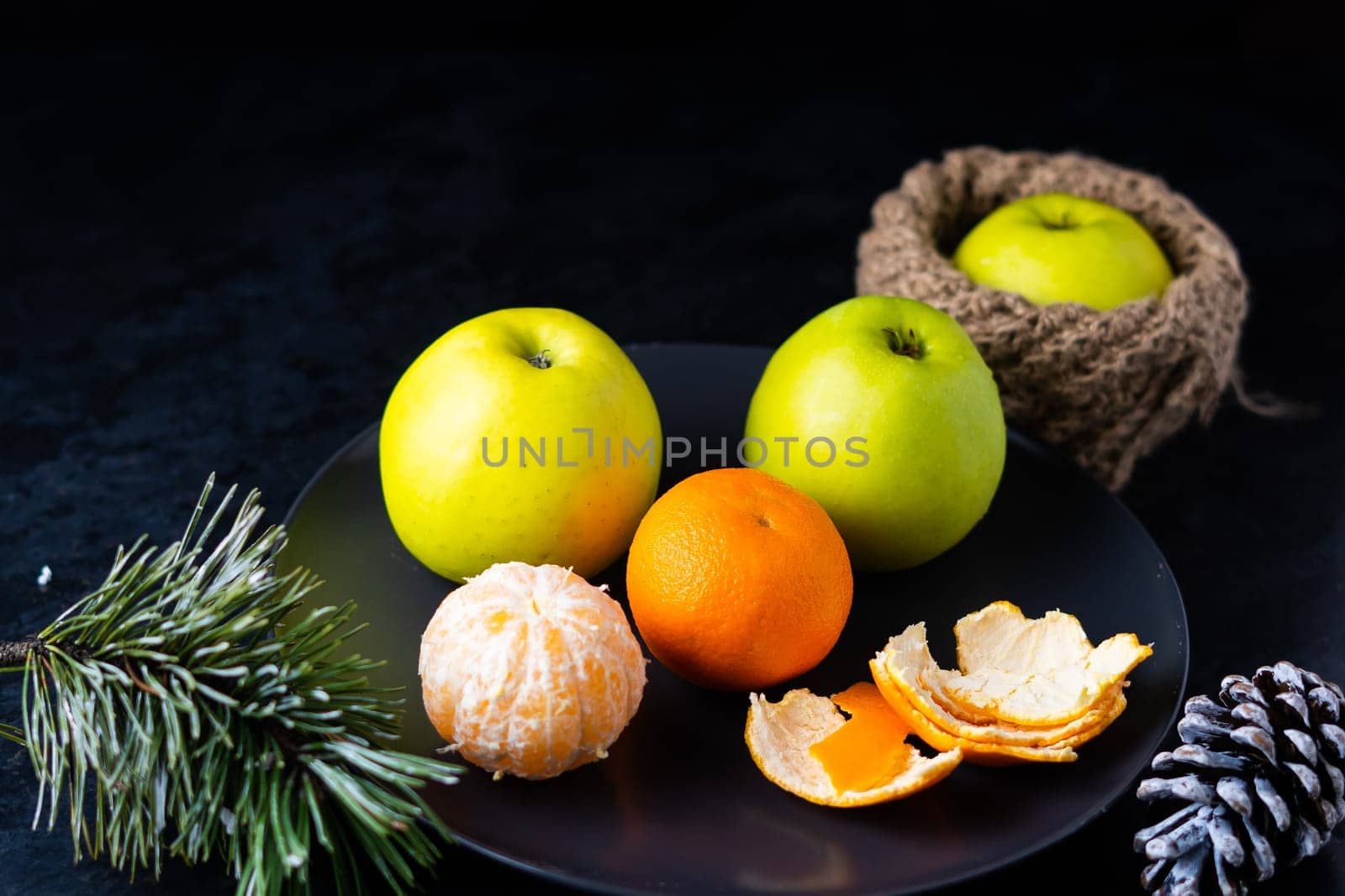 Green apples tangerines and pine cones on a table, dark background