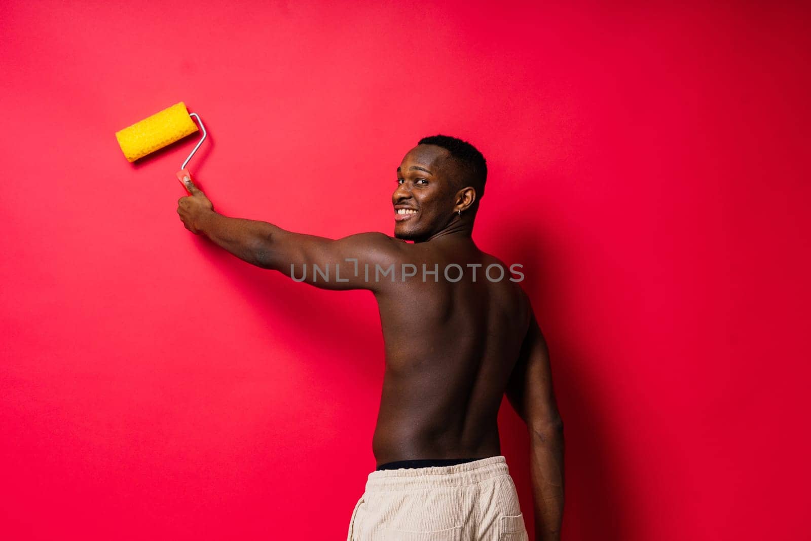 Happy construction worker holding paint roller performing interior renovation with an optimism.