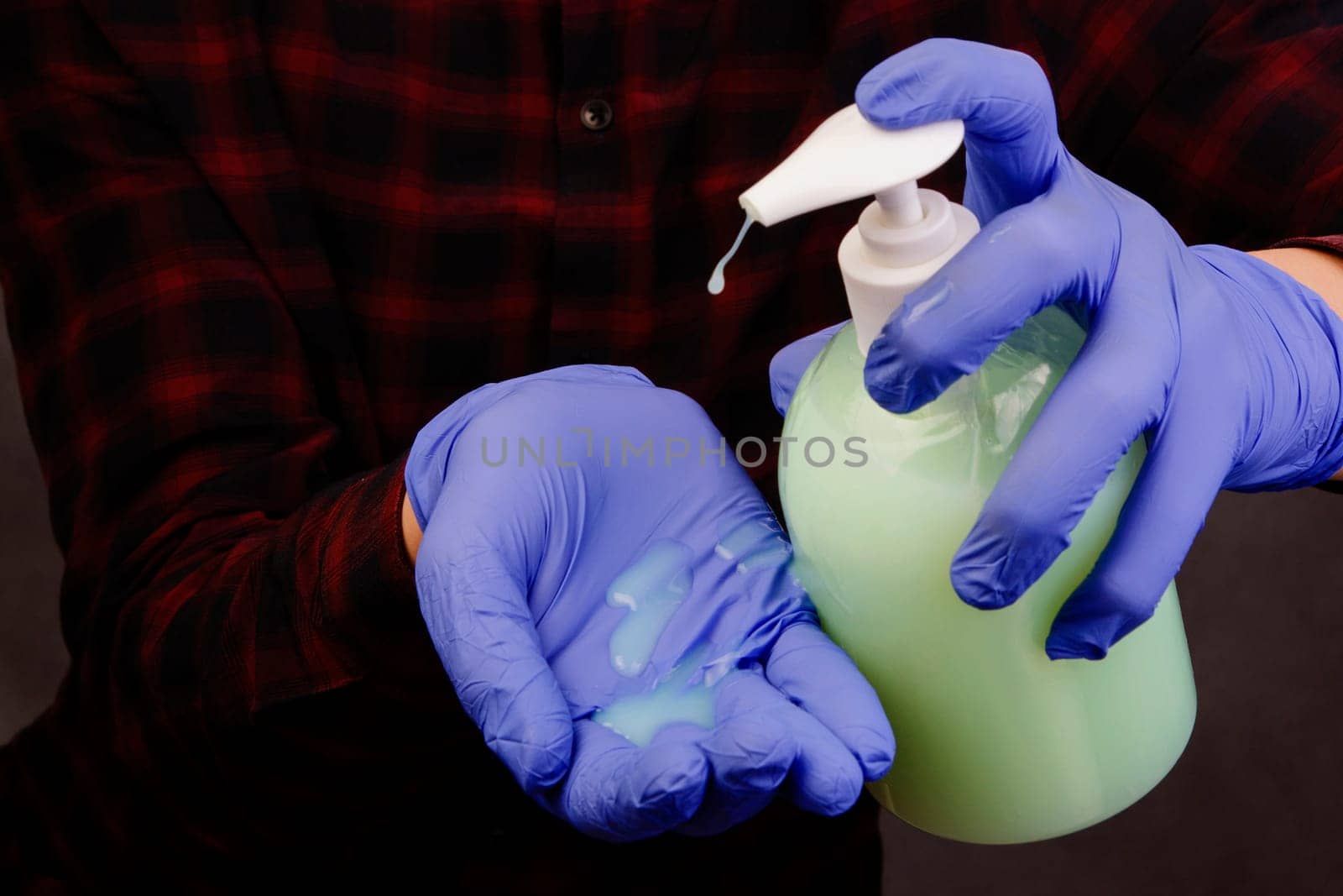 Hands in blue rubber gloves hold a plastic bottle of detergent and drip onto the palm.