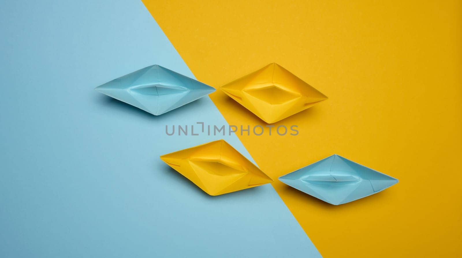 Paper boats on a yellow background, top view, representing the concept of unity and achieving common goals. Top view