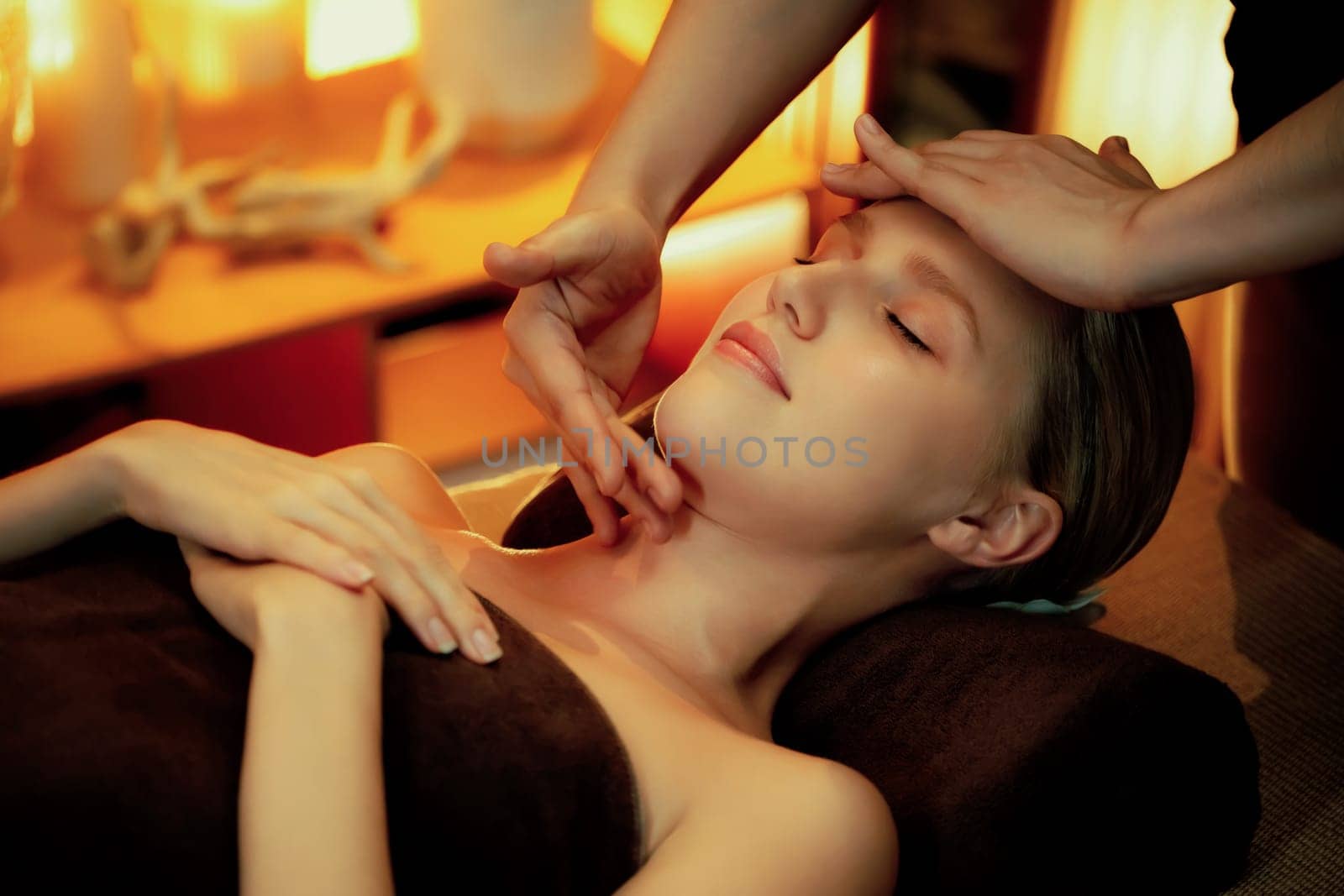 Caucasian woman enjoying relaxing anti-stress head massage and pampering facial beauty skin recreation leisure in warm candle lighting ambient salon spa in luxury resort or hotel. Quiescent