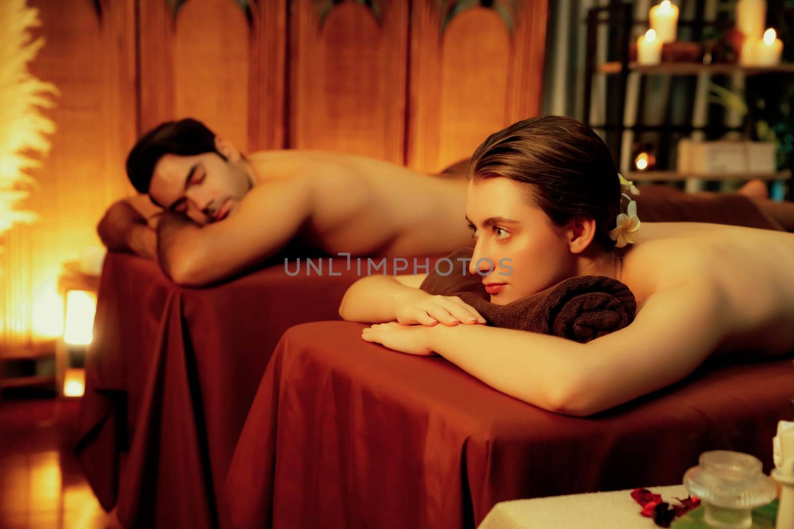 Caucasian couple customer enjoying relaxing anti-stress spa massage and pampering with beauty skin recreation leisure in warm candle lighting ambient salon spa at luxury resort or hotel. Quiescent