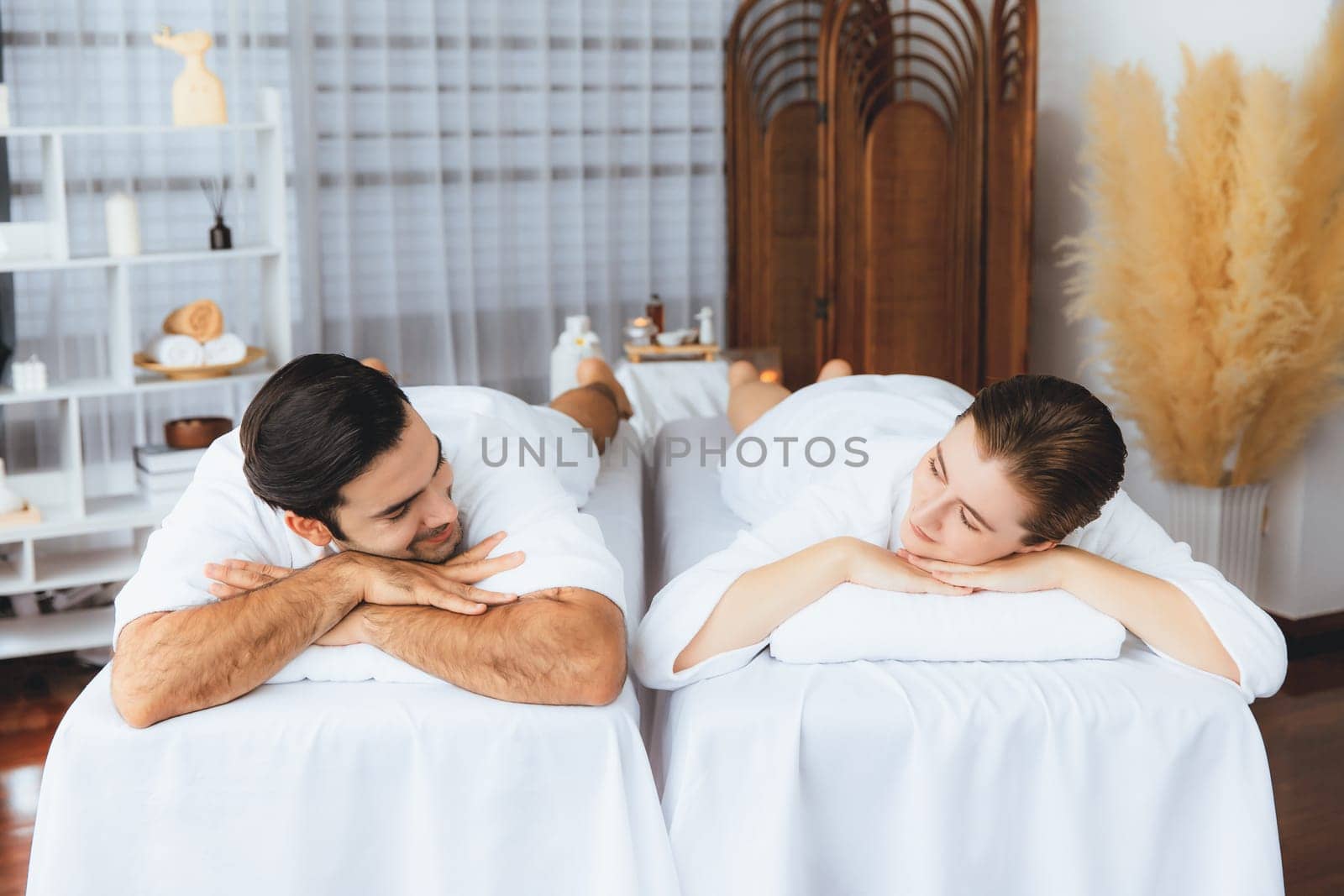 Caucasian couple customer enjoying relaxing anti-stress spa massage and pampering with beauty skin recreation leisure in day light ambient salon spa at luxury resort or hotel. Quiescent