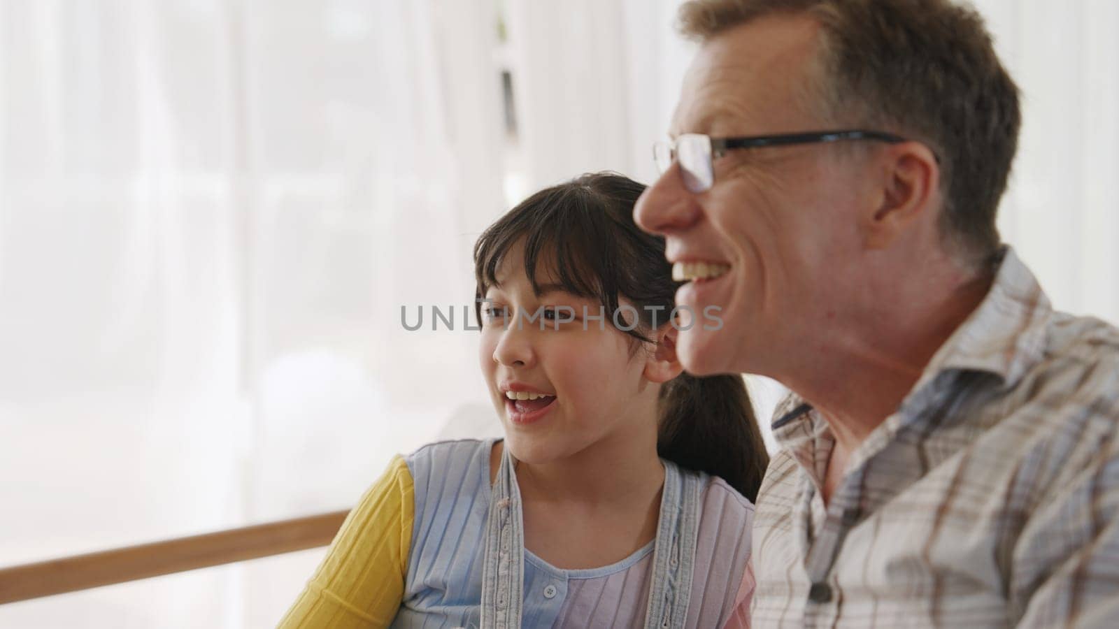Grandfather and granddaughter together watch interesting entertainment media on TV. Old senior use technology communicate with young generation cross generation gap strengthen family bond. Divergence.