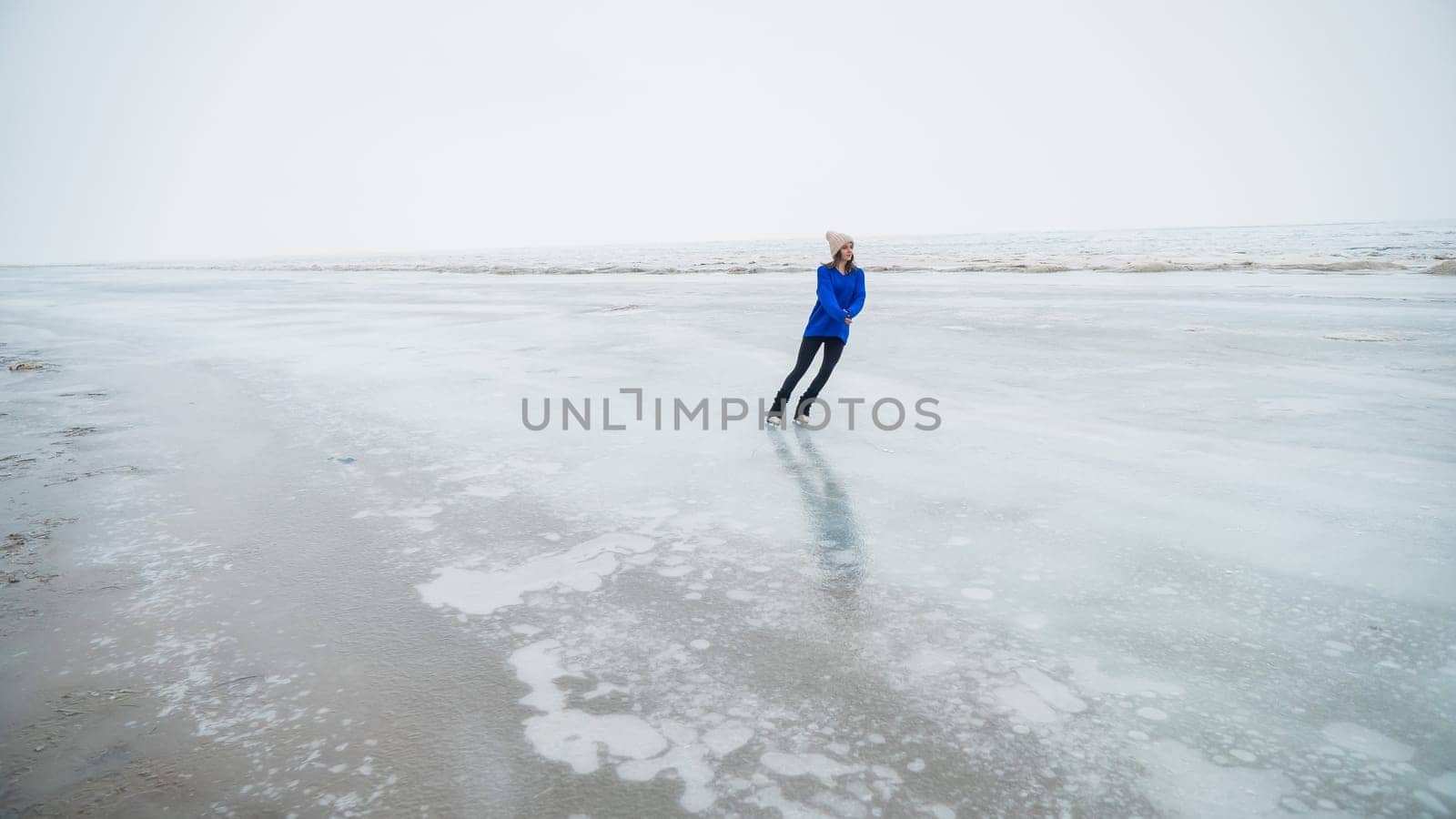 Caucasian woman in a blue sweater is skating on a frozen lake. The figure skater performs the program