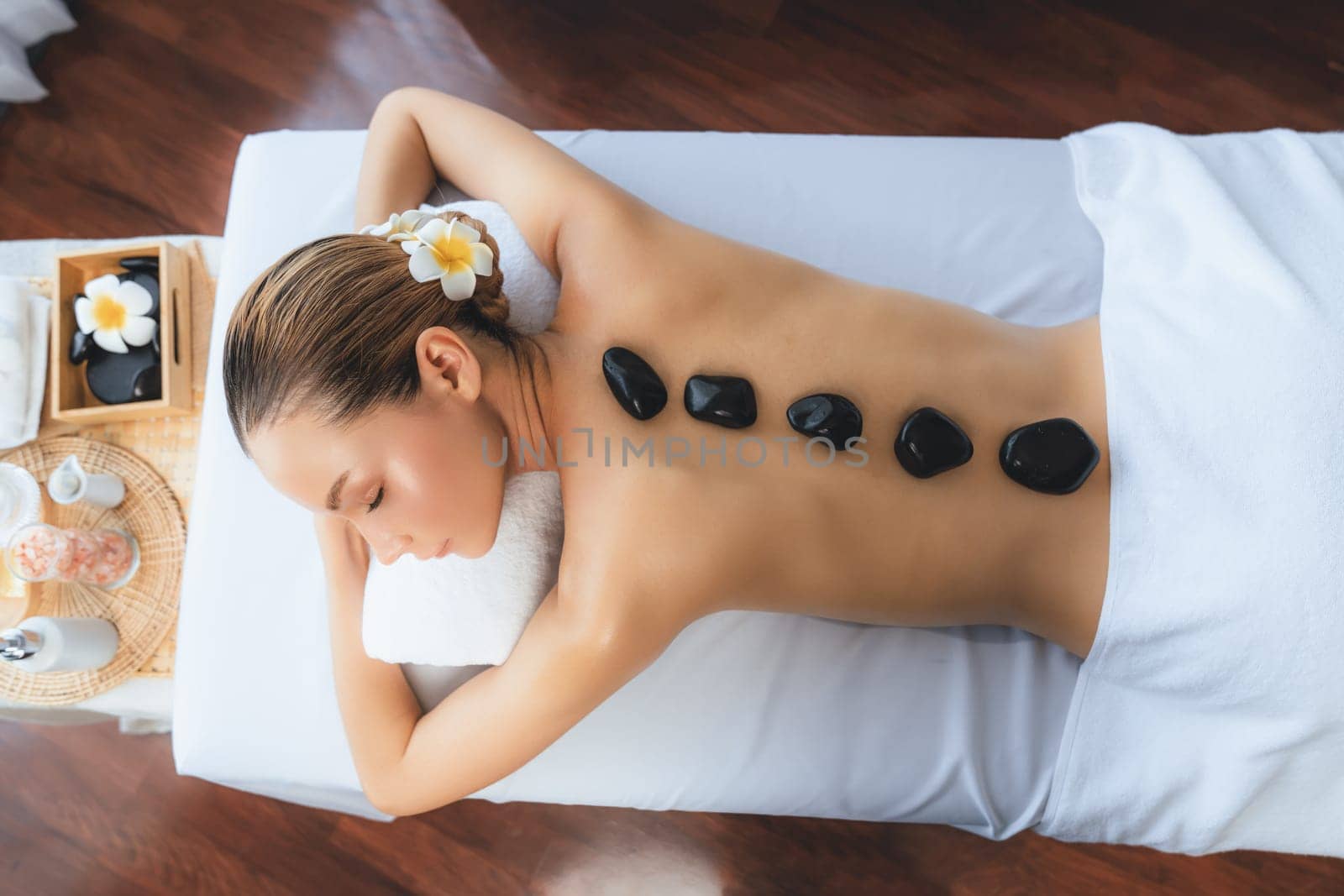 Panorama top view hot stone massage at spa salon in luxury resort with day light serenity ambient, blissful woman customer enjoying spa basalt stone massage glide over body. Quiescent