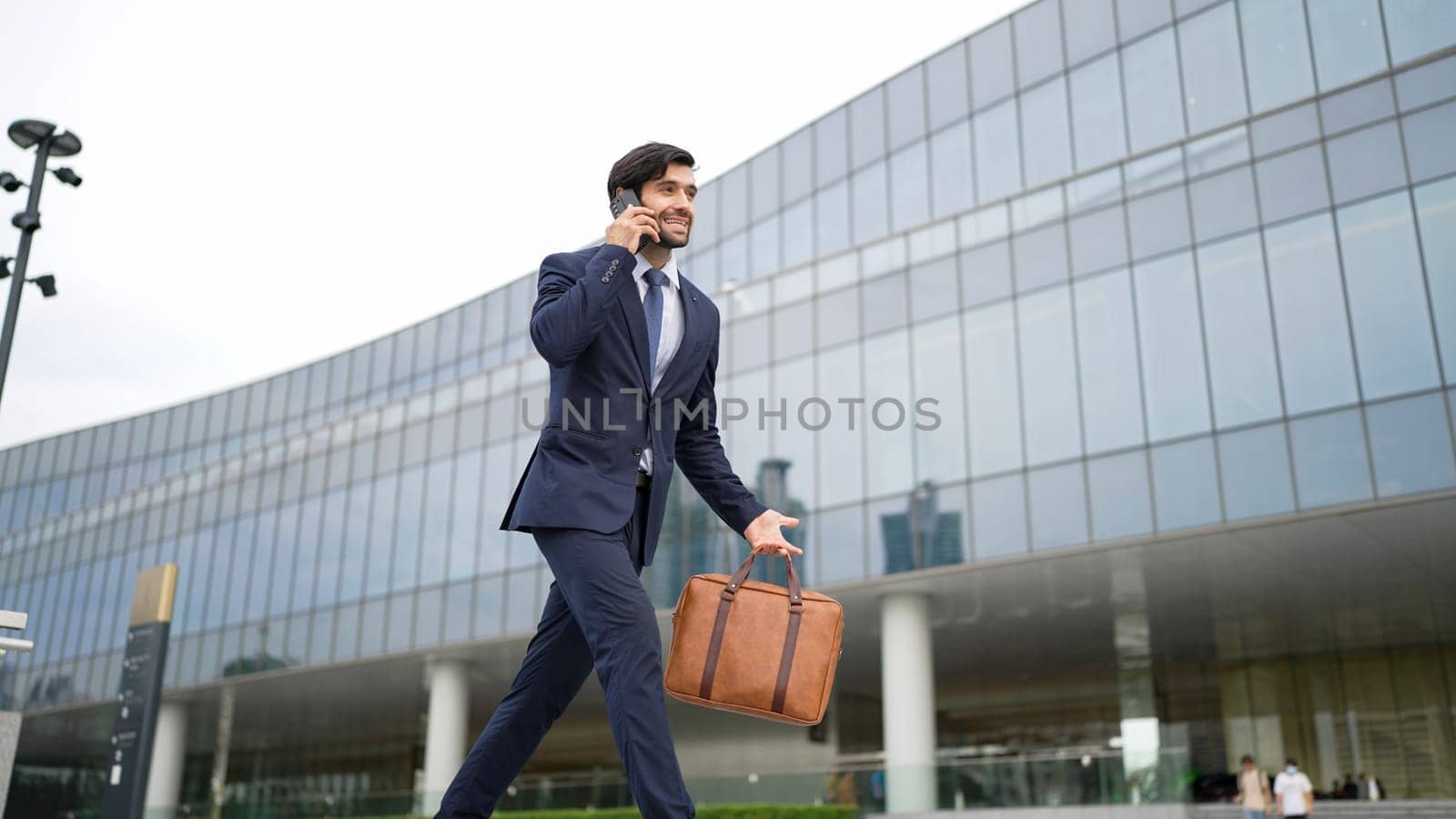 Smart business man using phone to talking while walking at building. Happy manager walking at street while talking on smart phone to discuss business plan or marketing strategy or working. Exultant.