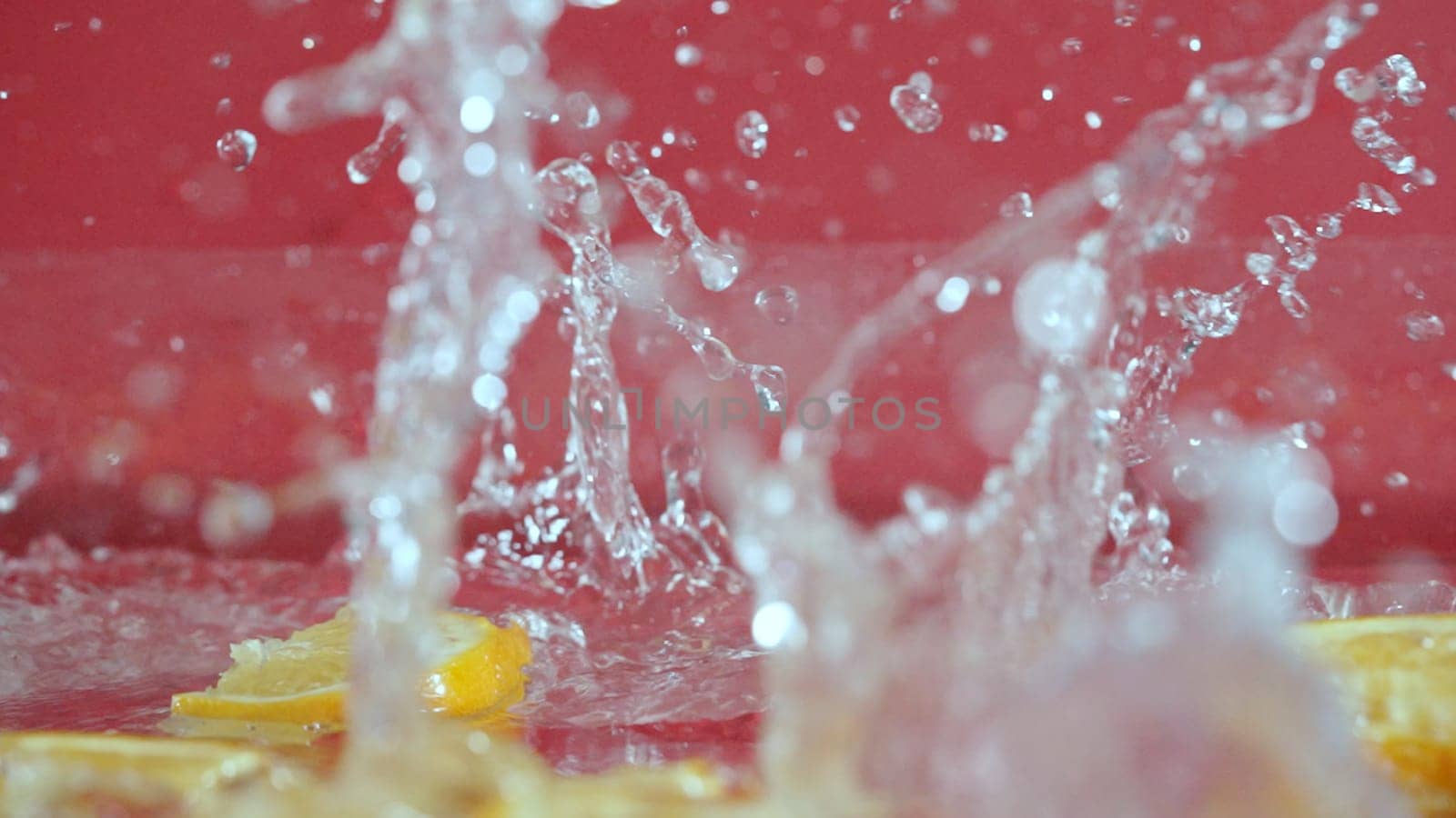 Close up of fresh lemon slices splashing on red background. Macro of sliced lemon dropping and falling in to splashing water. Freshness and hydration concept. Citrus. Design for poster. Pabulum.