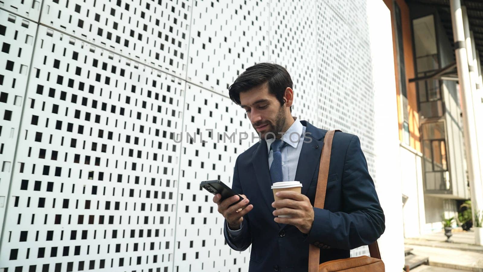 Smart manager looking at mobile phone and walking at street while wearing suit. Skilled investor looking mobile phone to checking sales or working while holding coffee cup. White background. Exultant.