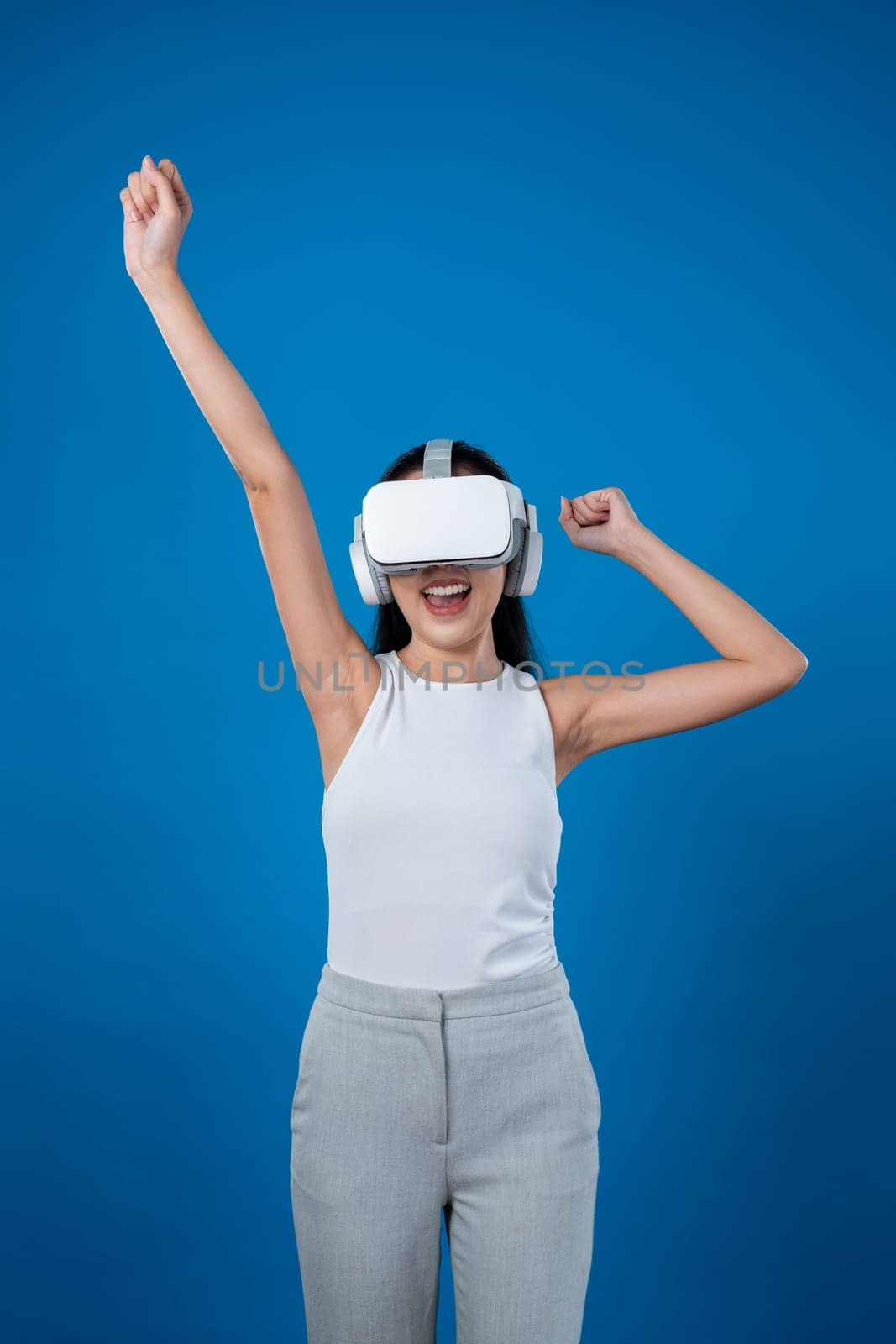 Smart female standing with blue background wearing VR headset connecting metaverse, futuristic cyberspace community technology. Elegant woman excited seeing generated virtual scenery. Hallucination.