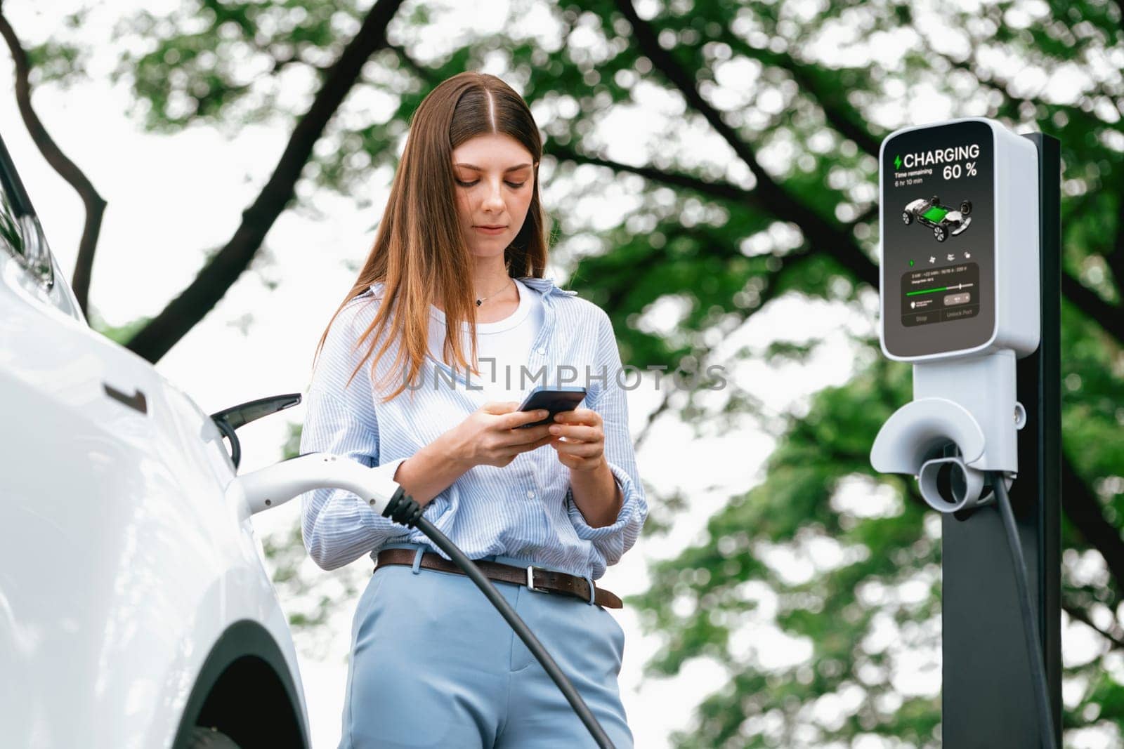 Young woman using smartphone to pay for electric car charging. Exalt by biancoblue