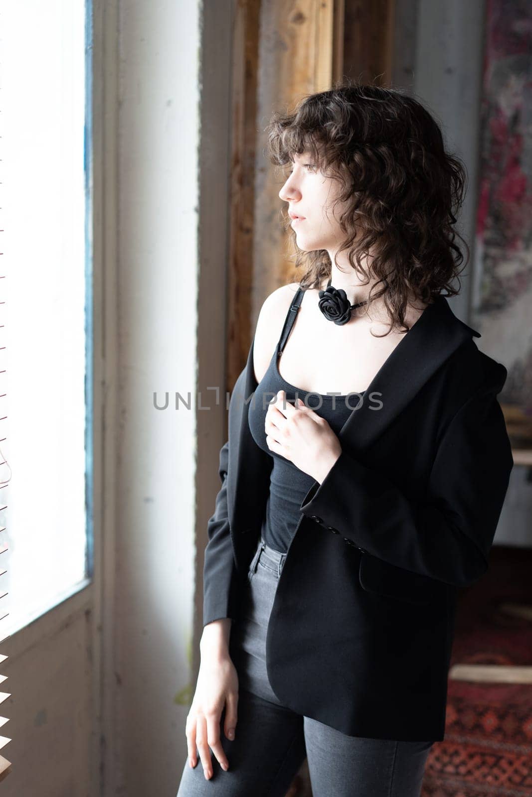 young beautiful woman posing in the studio, standing in black clothes near the window