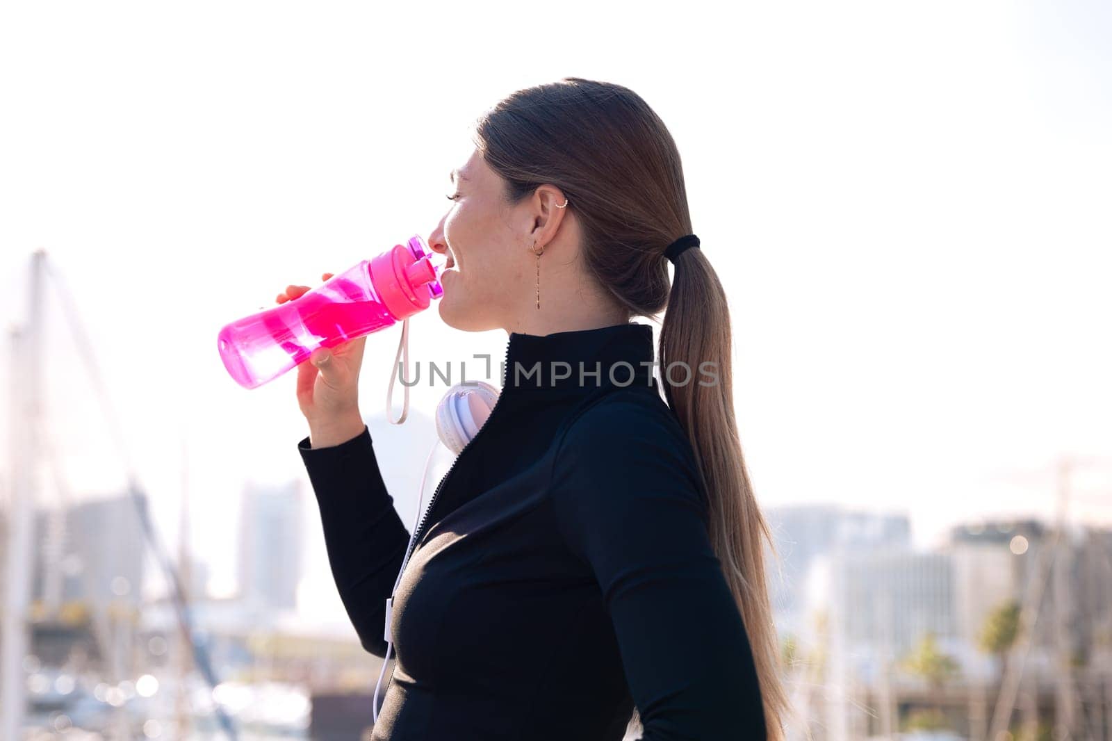 Side view runner girl drinking water from a sports bottle outdoors.Vertical by molesjuny