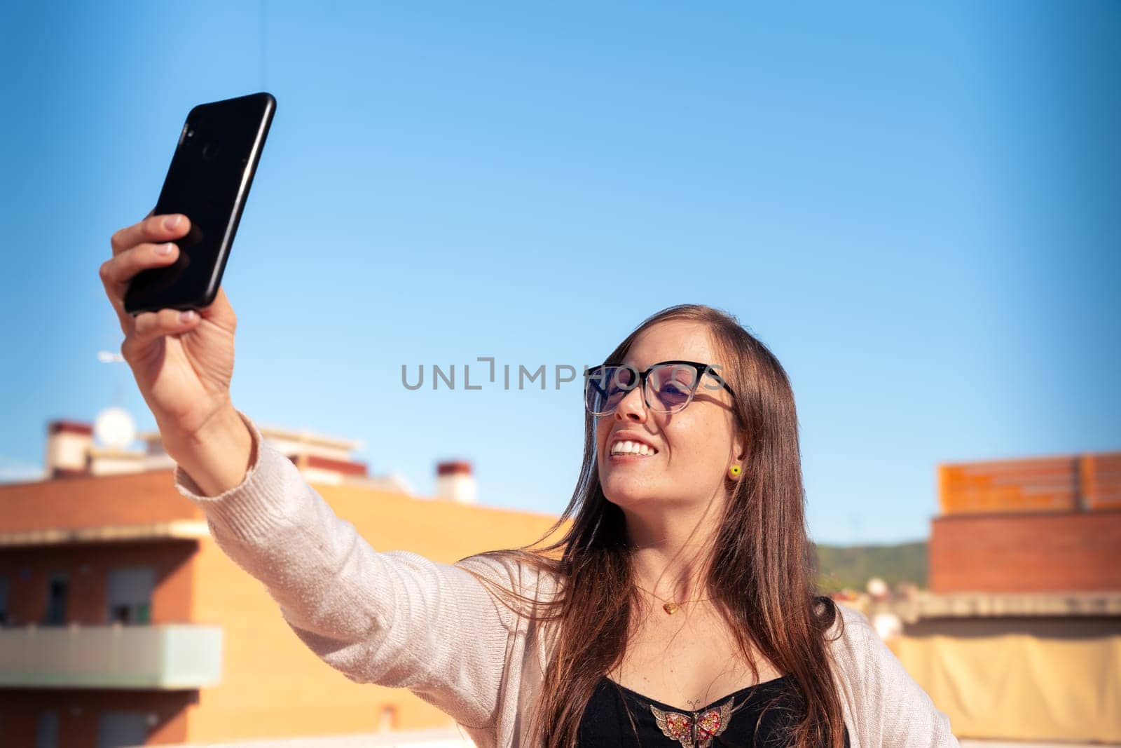 Young caucasian woman taking a selfie with cell phone and smiling outdoors. by mariaphoto3