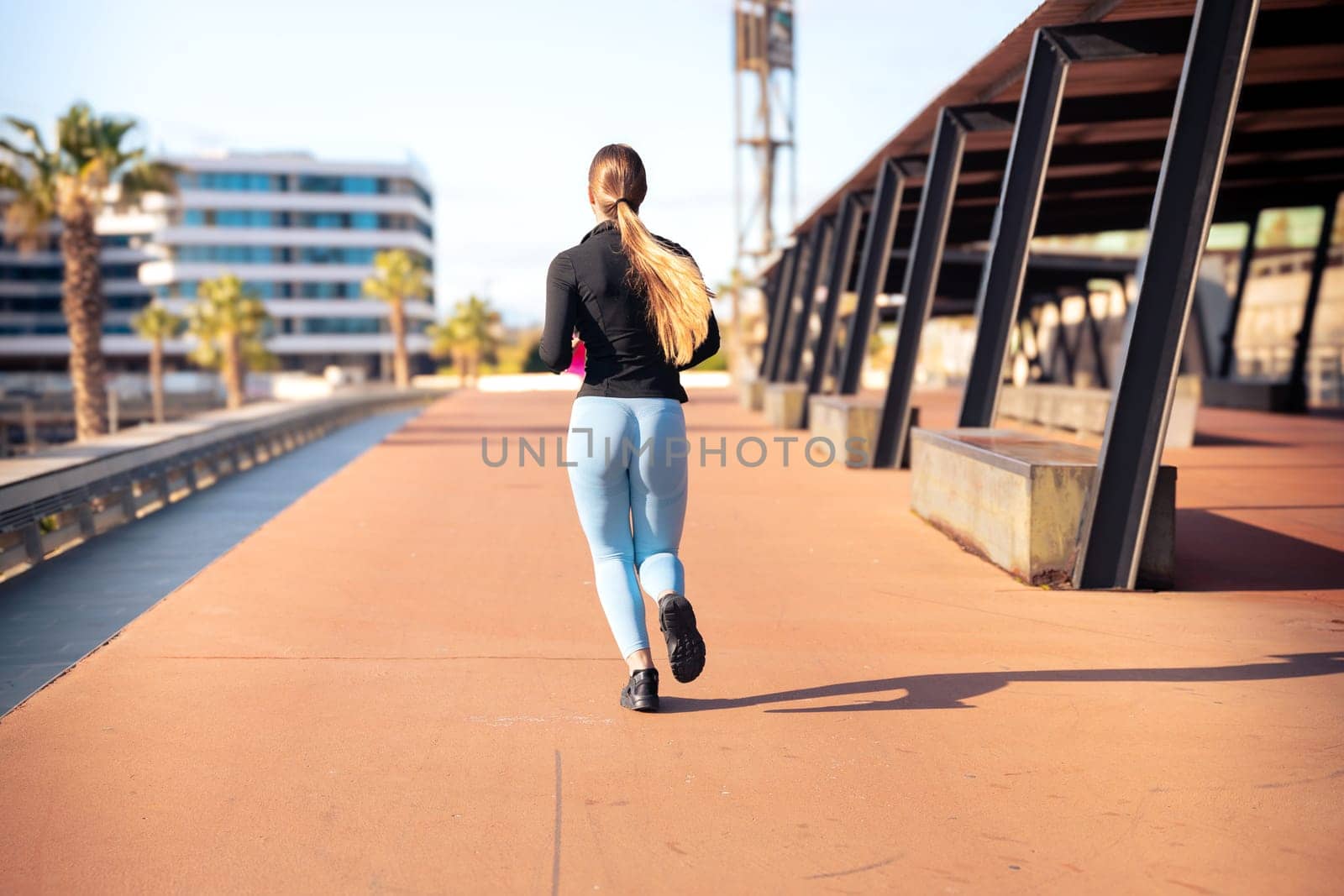 Rear view a young runner with water bottle in hand trains around the city. by mariaphoto3