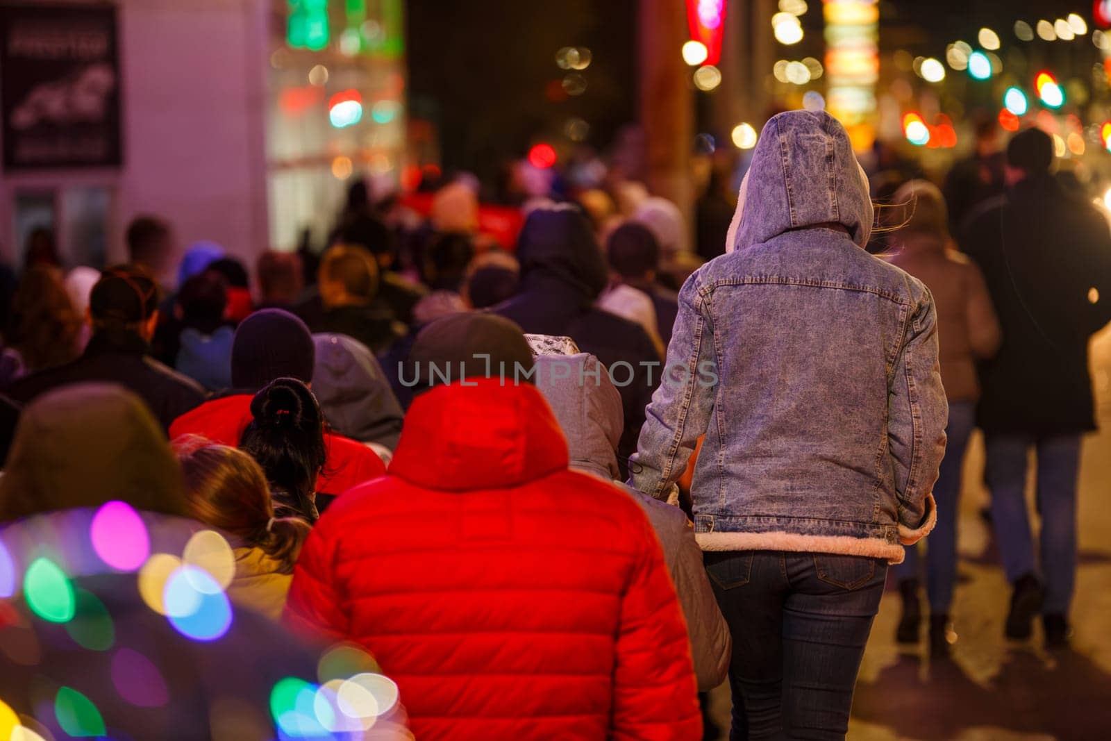 crowd of people with warm clothes are walking along the city street sidewalk at night after celebration event