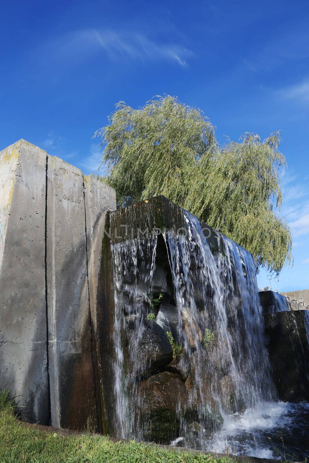 A waterfall against a background of a tree on the river bank against a blue sky, view from below.