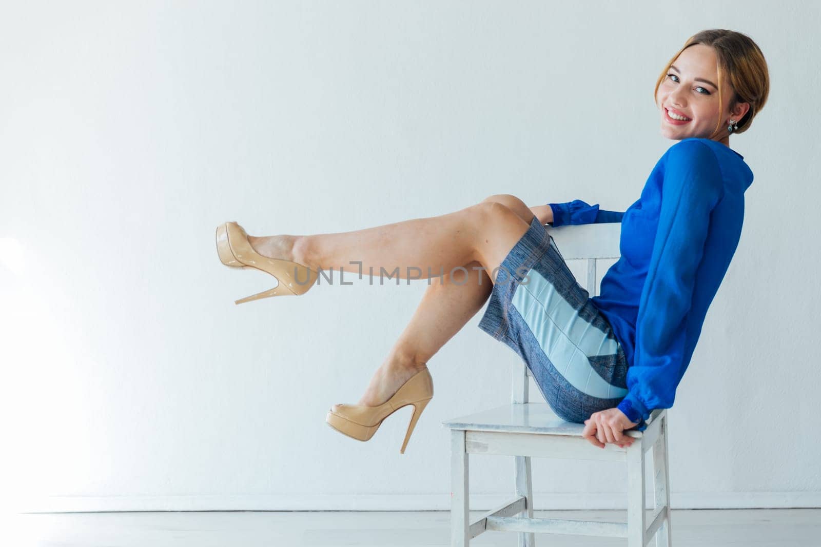 a woman in blue clothes sits on chair against a white wall