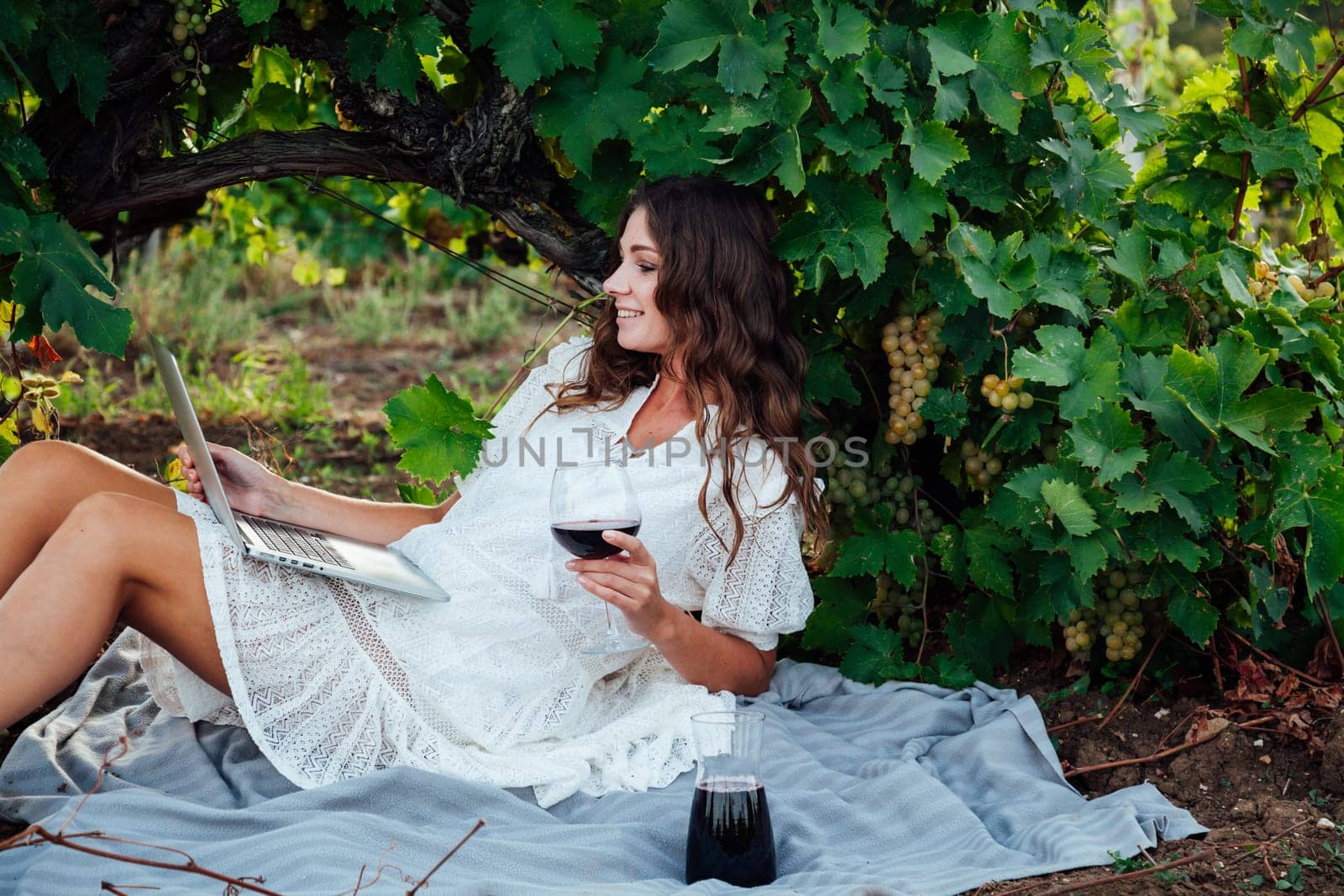 a woman sits on a mat in grape leaves with a glass of wine