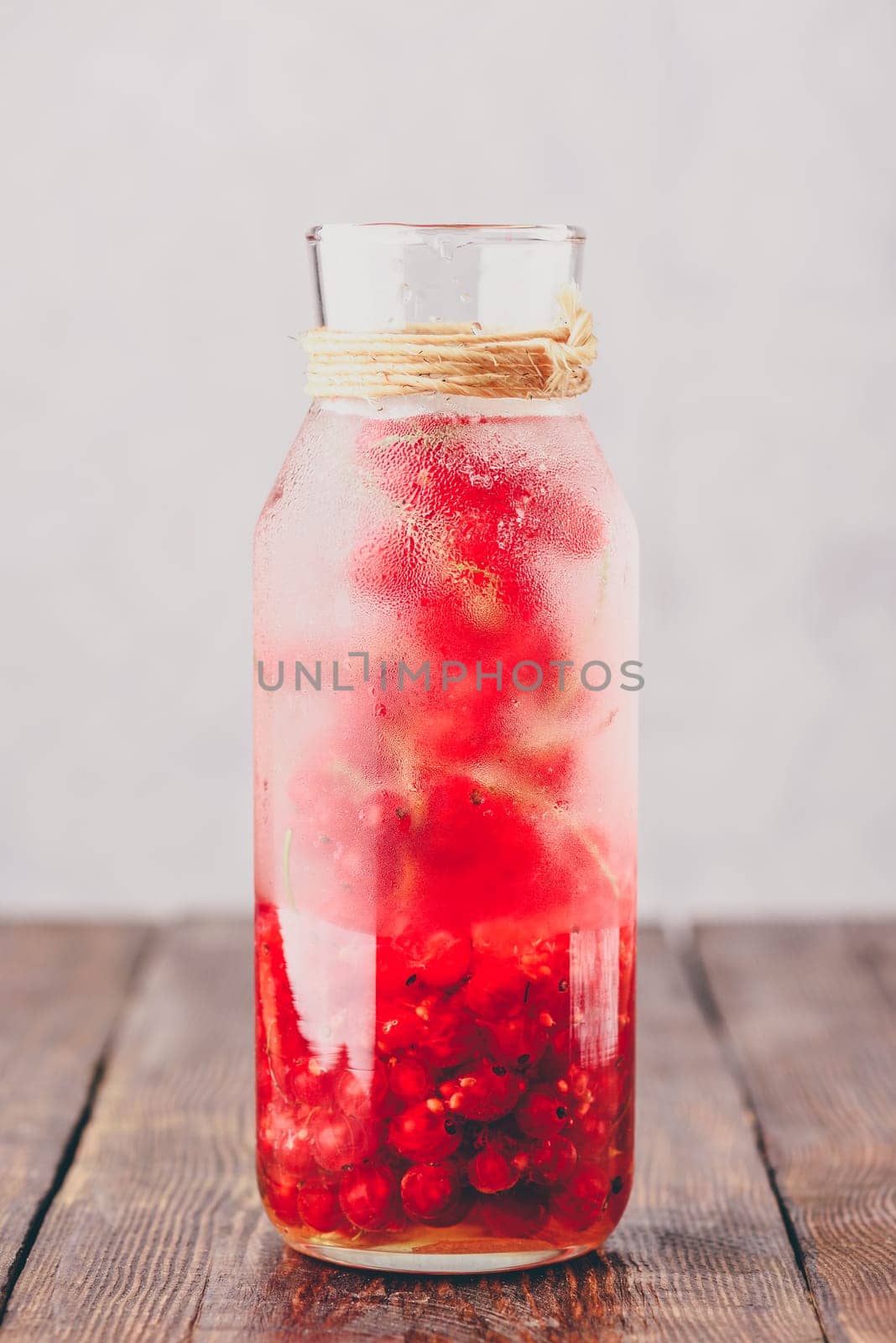 Red currant infused water with ice in glass bottle