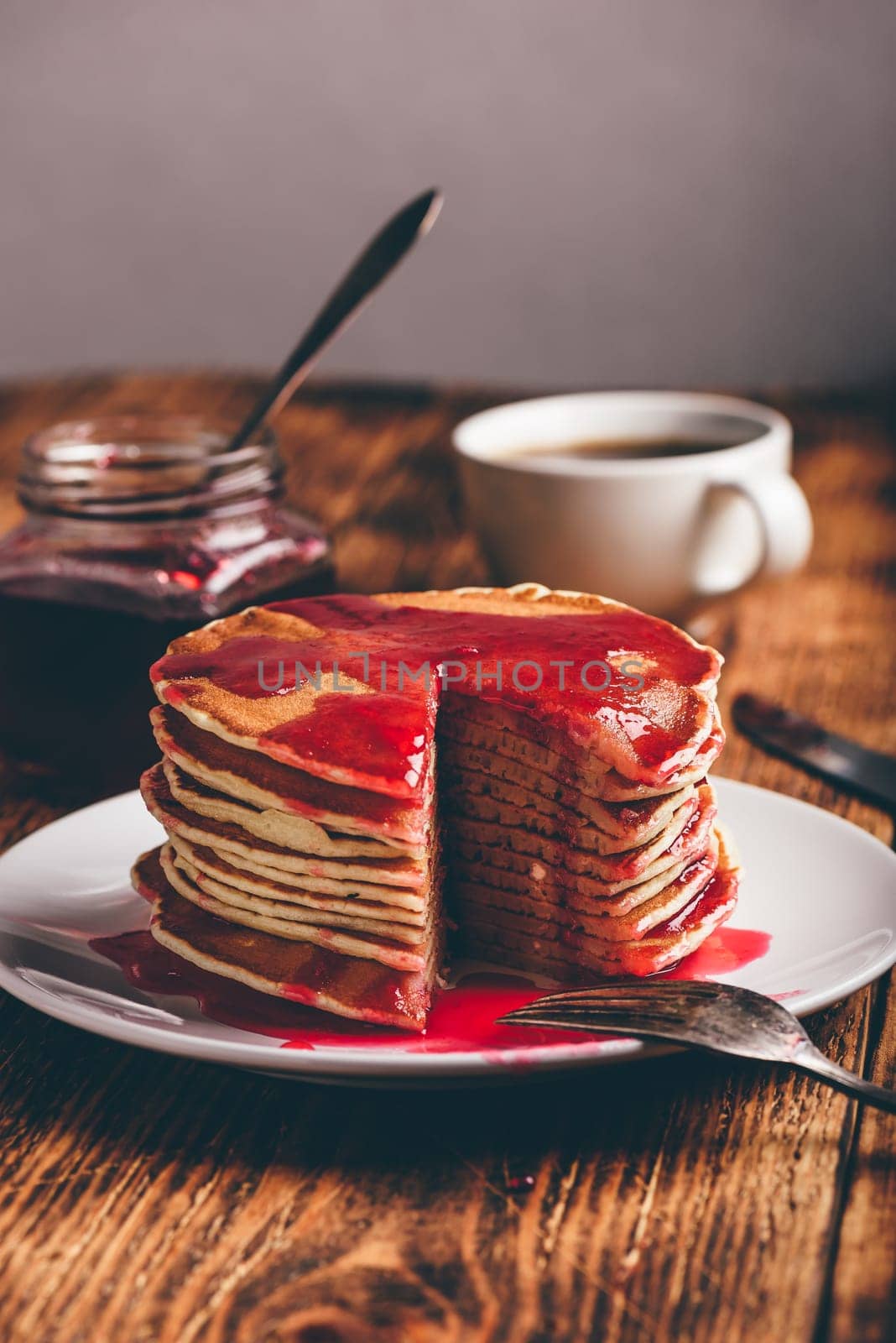 Stack of pancakes with berry jam on white plate over wooden table