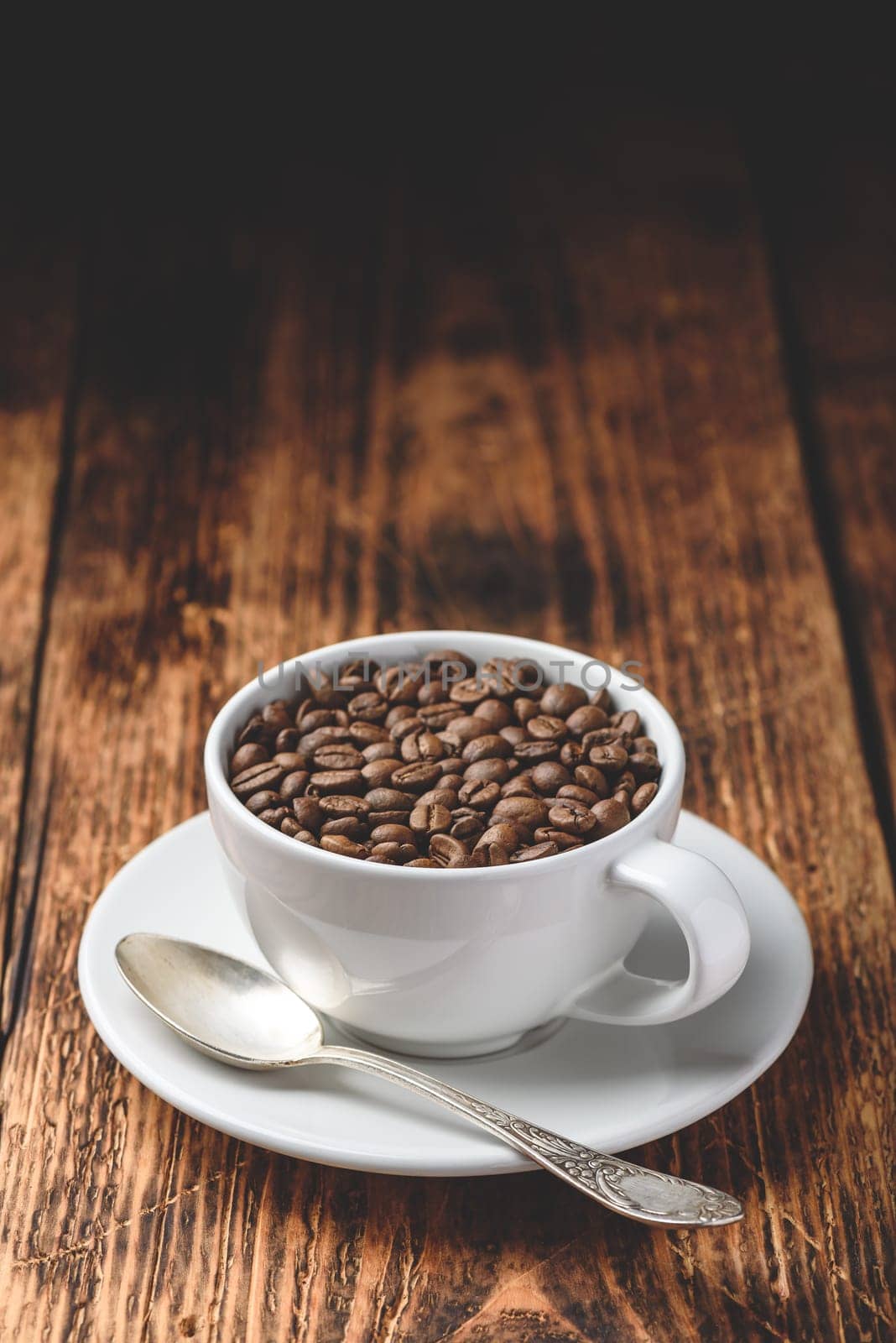 Roasted coffee beans in white cup over rustic wooden surface