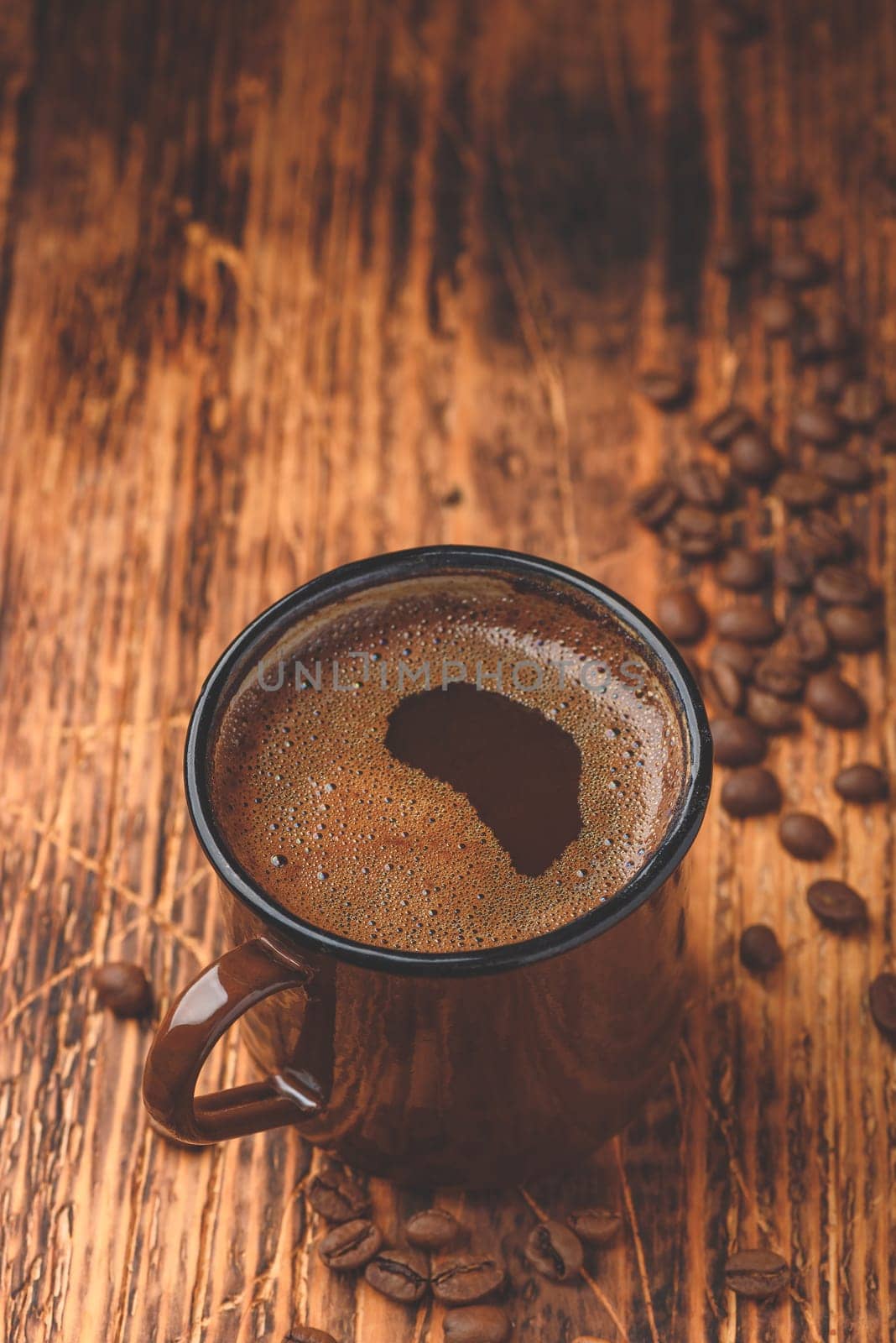 Brewed black coffee in metal mug over wooden surface