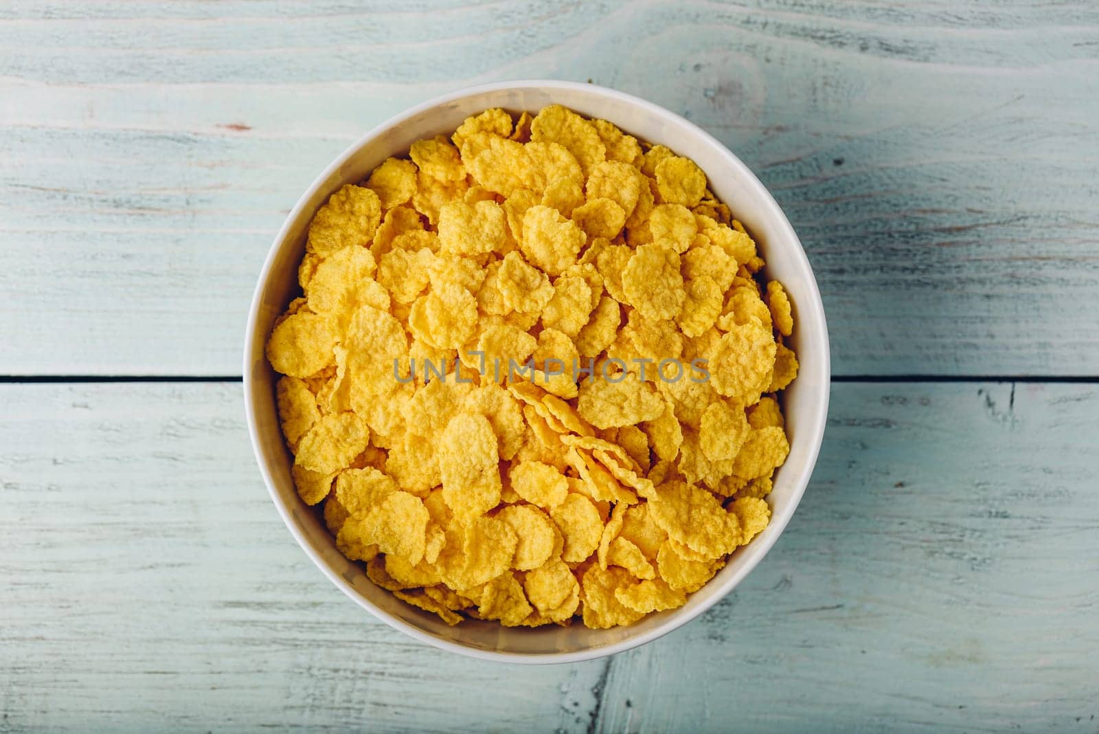 White bowl of corn flakes on a wooden surface