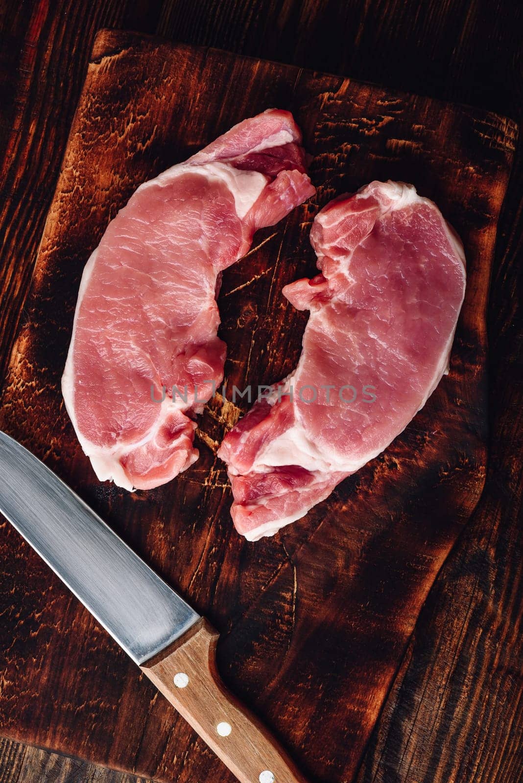 Two pork loin steaks with knife on rustic cutting board