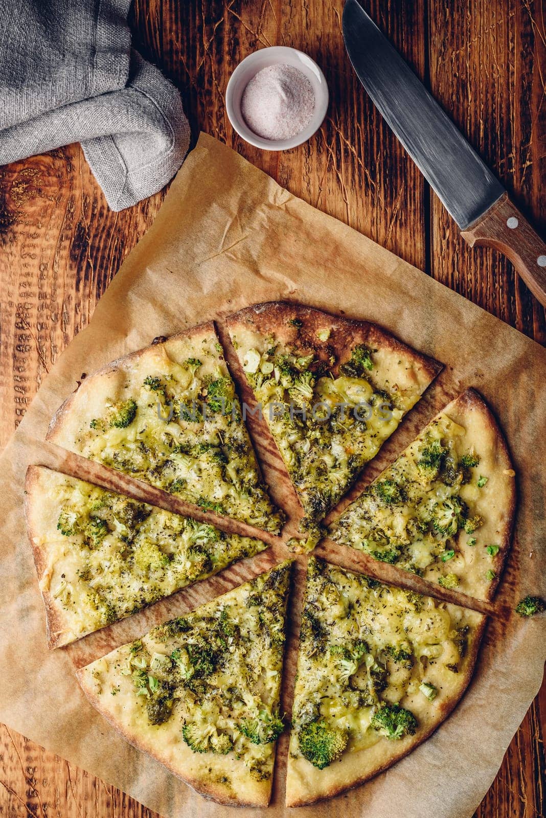 Sliced homemade pizza with broccoli, pesto sauce, herbs and cheese on baking paper. View from above