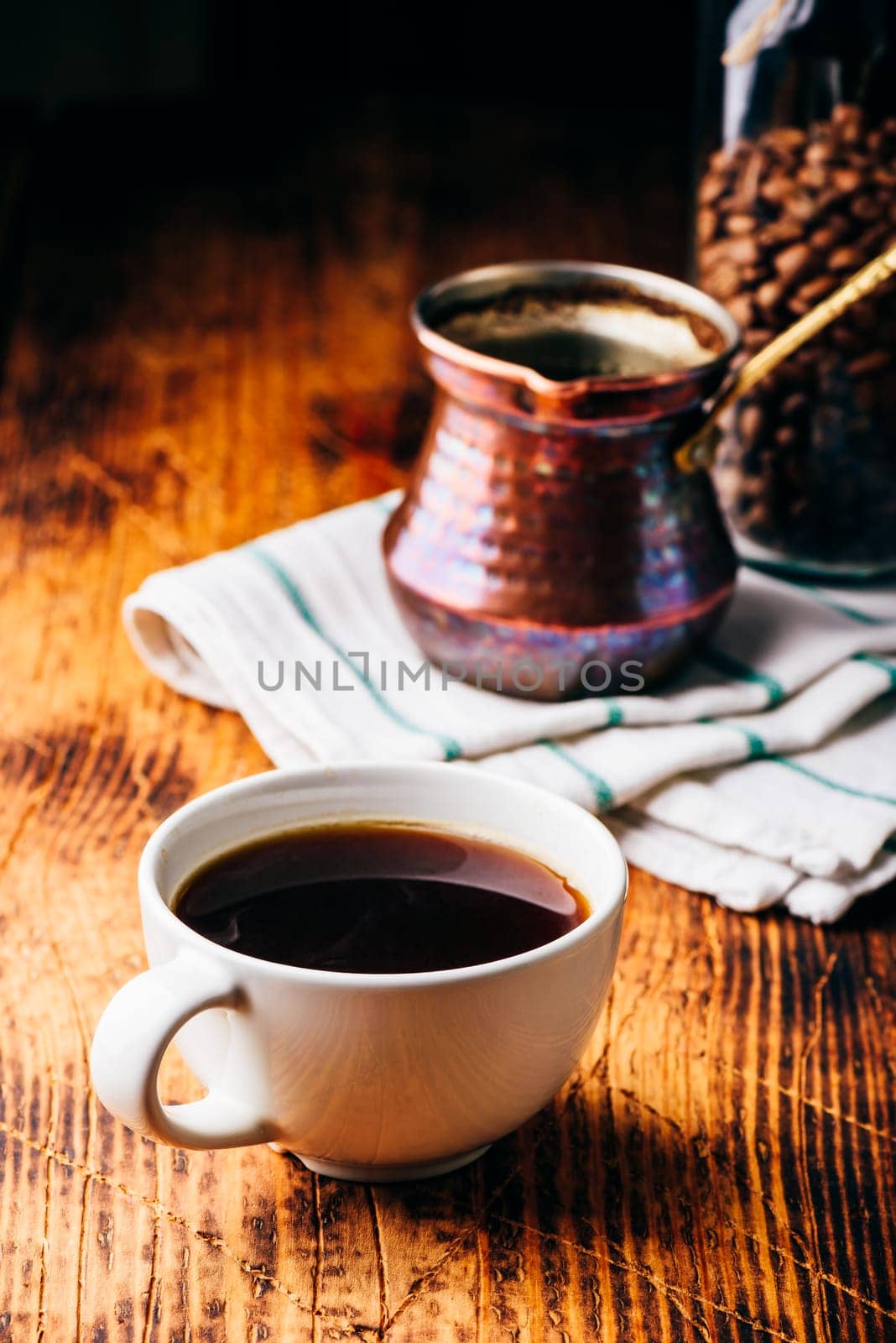 Cup of turkish coffee with copper cezve and jar of roasted coffee beans on wooden table