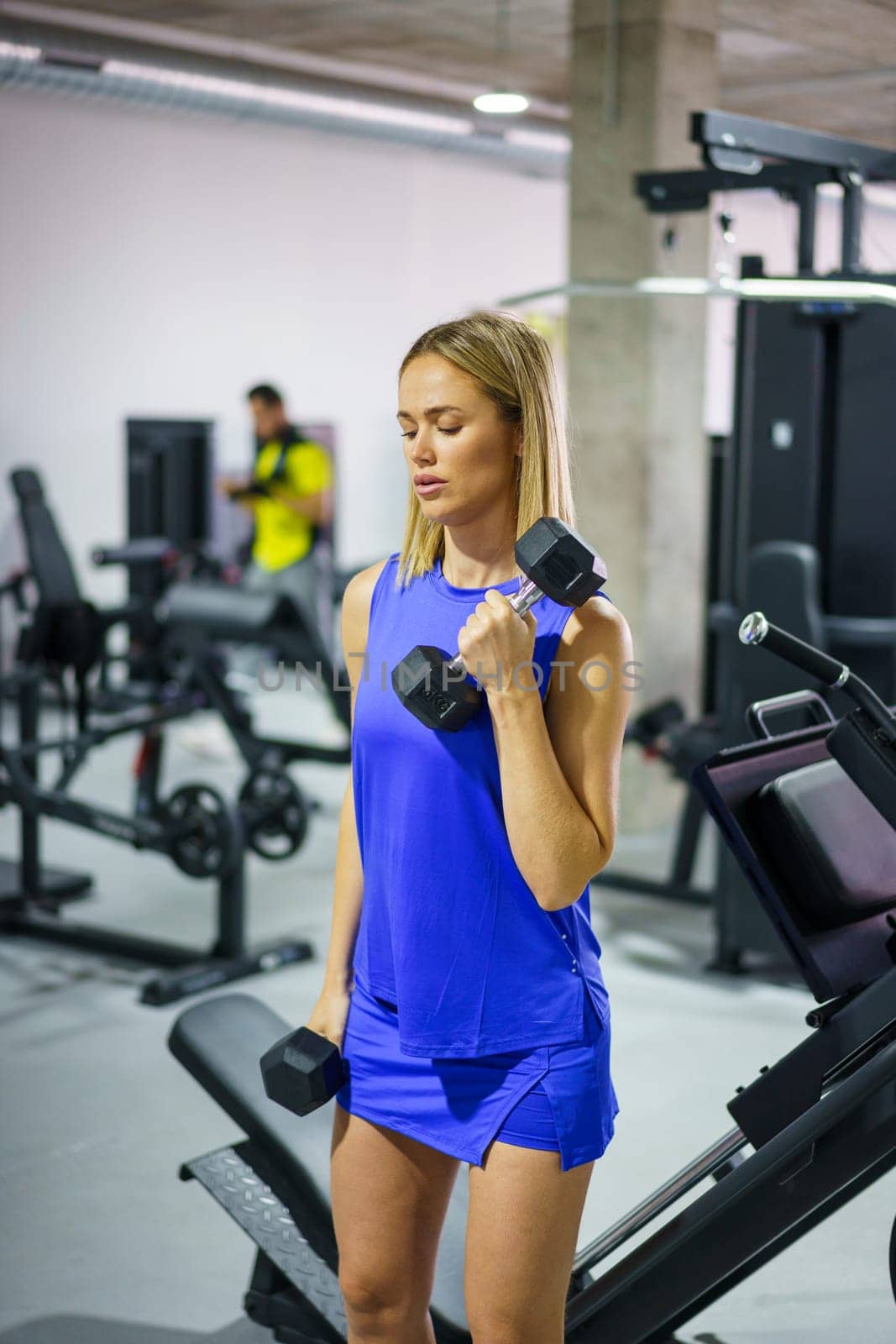 Vertical photo of an active young caucasian woman having an weightlifting workout at the gym