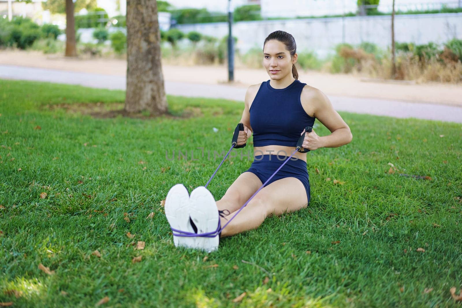 A young woman is working out in the park using a resistance band to exercise her body and maintain fitness by javiindy