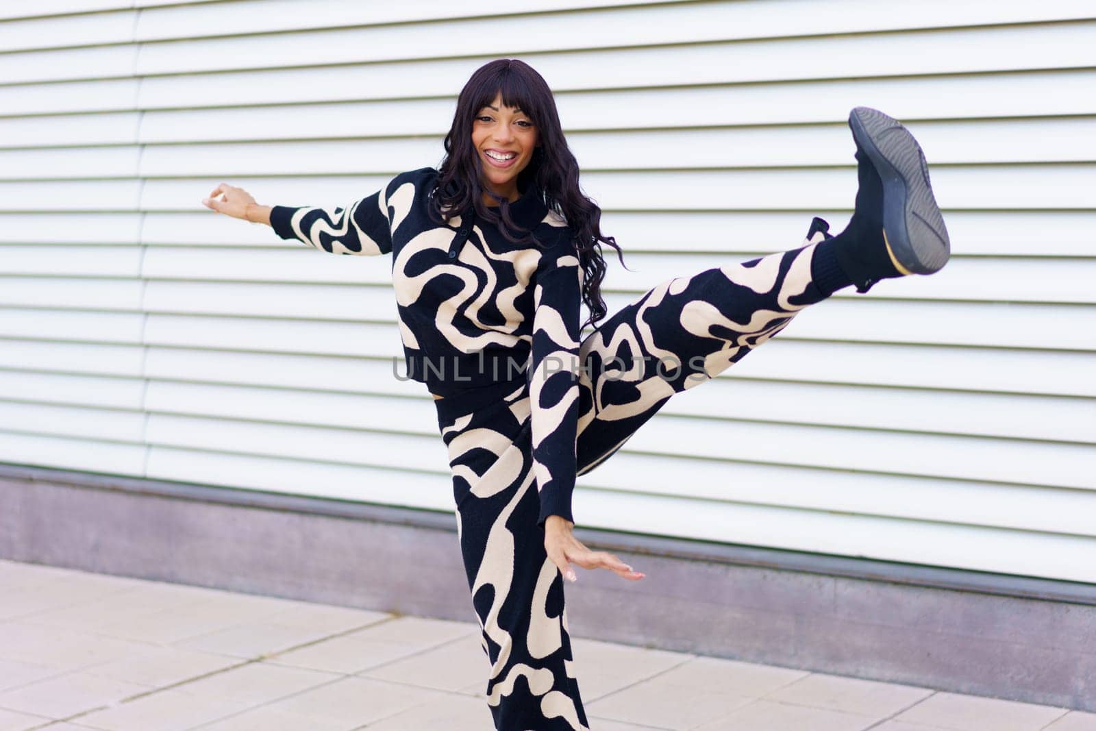 Energetic beauty woman with modern black and white clothes smiling and dancing in the city