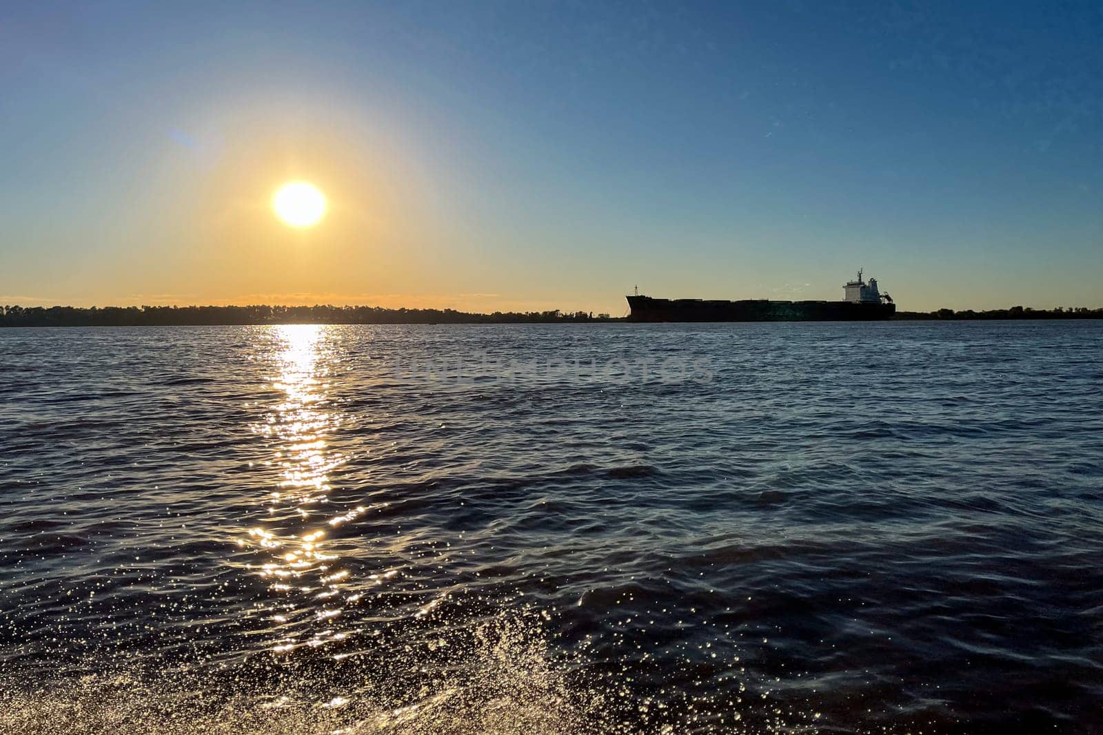 The Parana river at sunset, a cargo ship and the city in the backlit background by VeroDibe