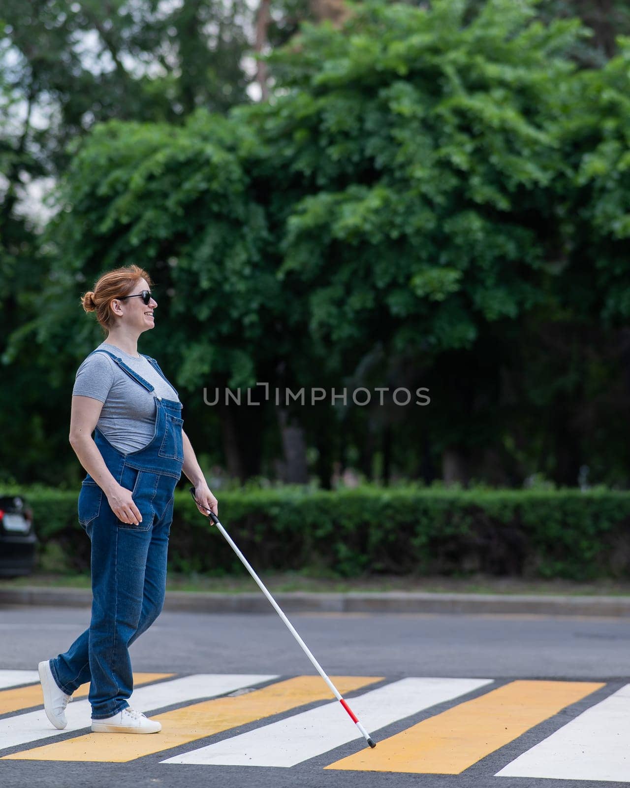 Blind pregnant woman crosses the road at a crosswalk with a cane. by mrwed54