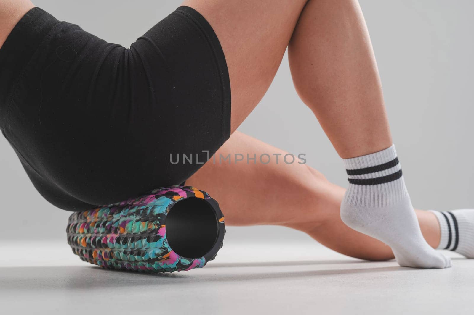 Faceless woman doing roller exercise for myofascial release on white background. Self-massage of thighs