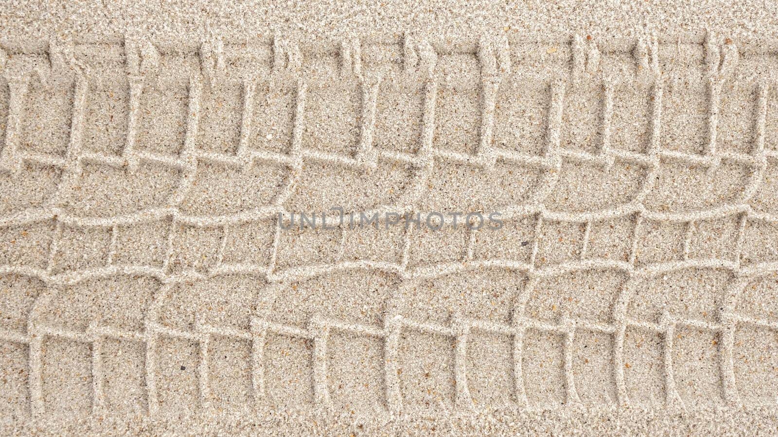 A serene image captures a single tire track delicately etched on the sandy shore, blending human touch with natures beauty in a harmonious display of contrast and tranquility.