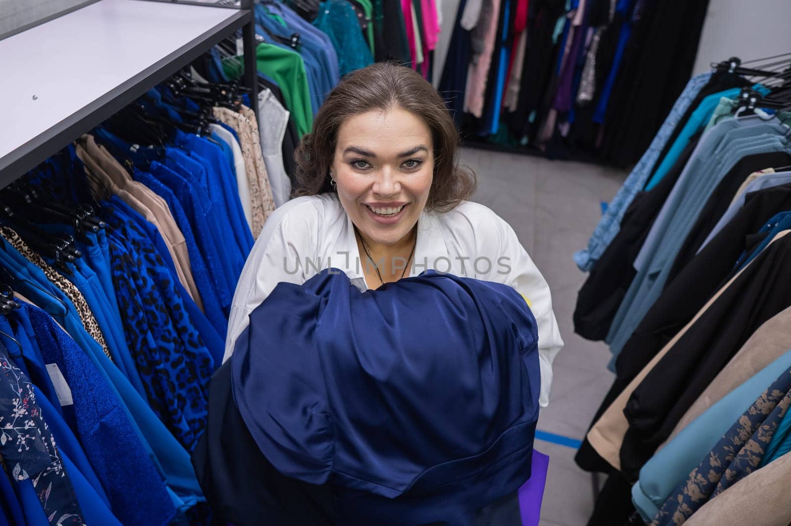 Top view of a chubby-cheeked woman holding an armful of clothes in a plus size store