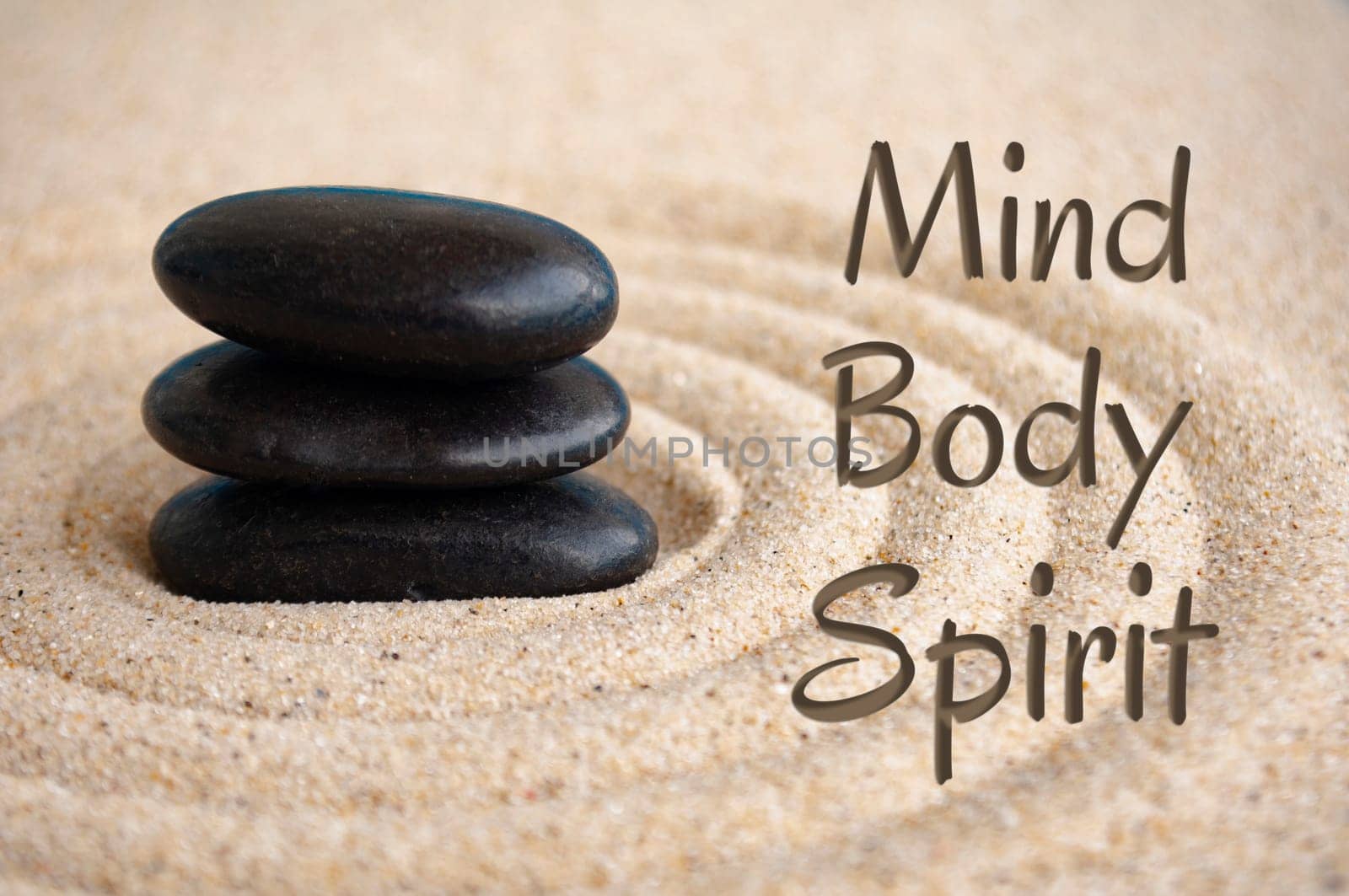 Mind, body and spirit text with black Zen stones on sand background.