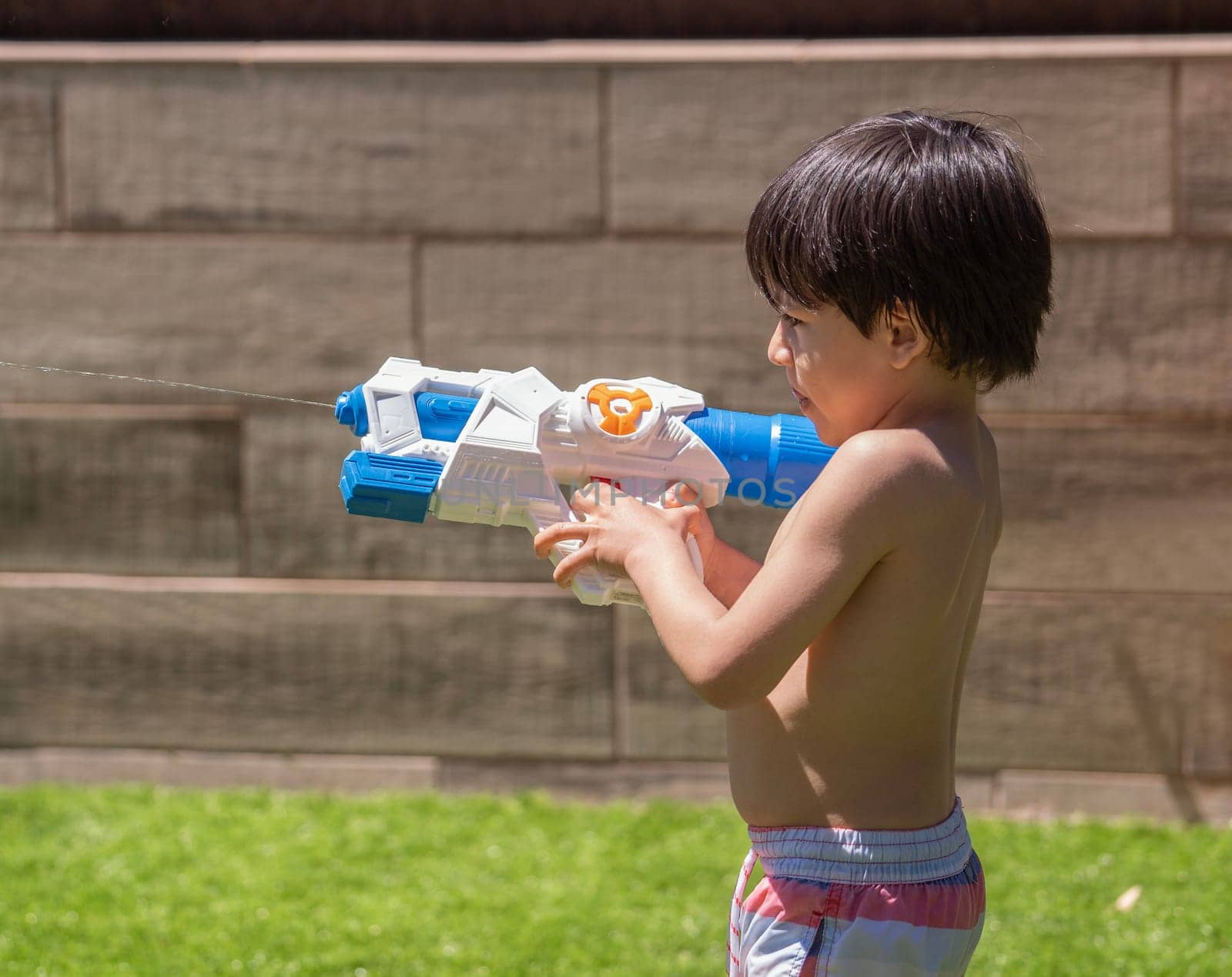 Side view of a kid playing with a toy gun in swimsuit in hot summer holidays.