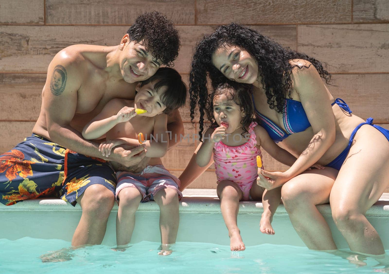 Cheerful dominican family of four enjoying summer holidays in a pool.