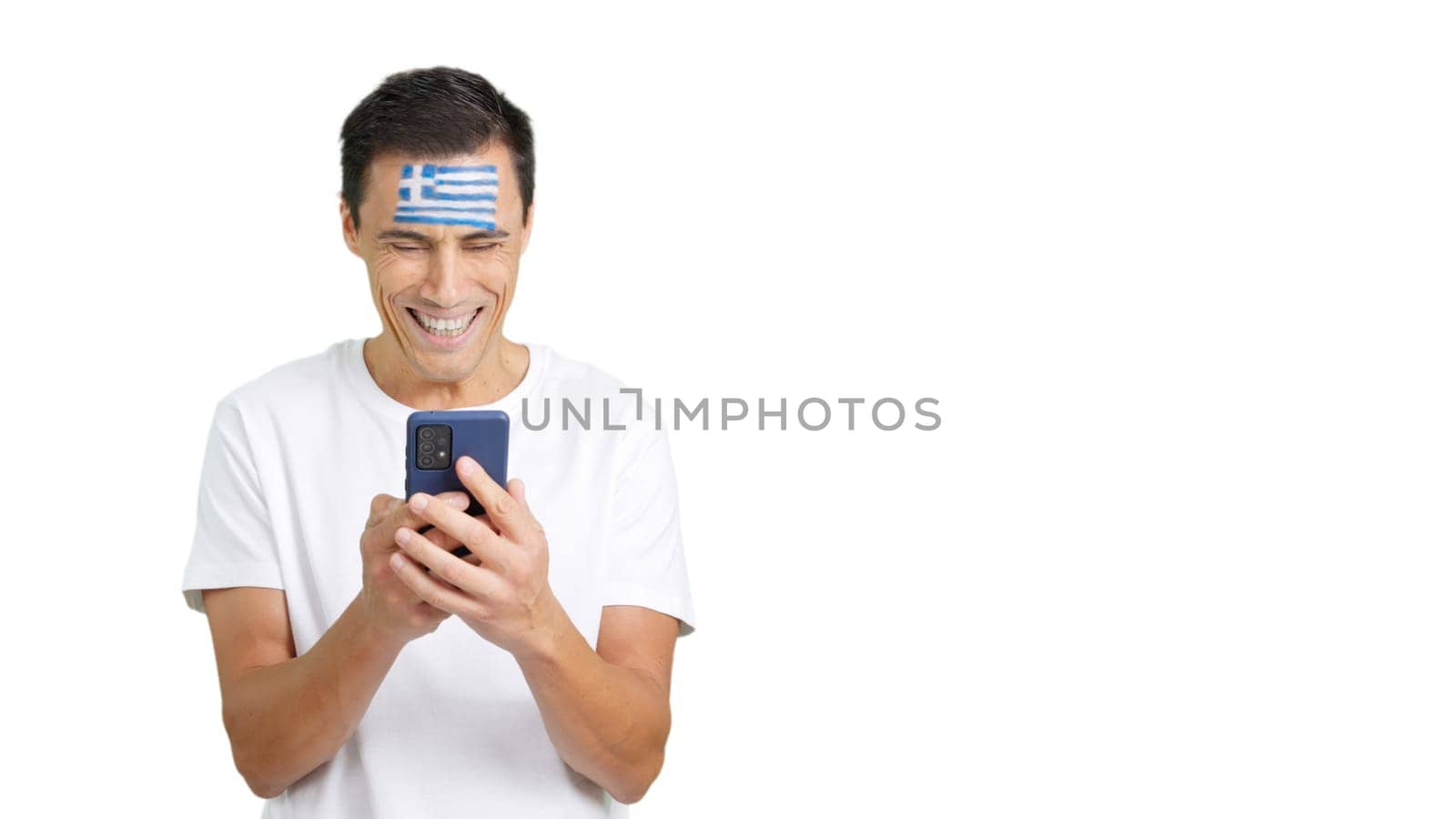 Greek supporter with the flag of Greece painted on his face, looking at his mobile phone smiling